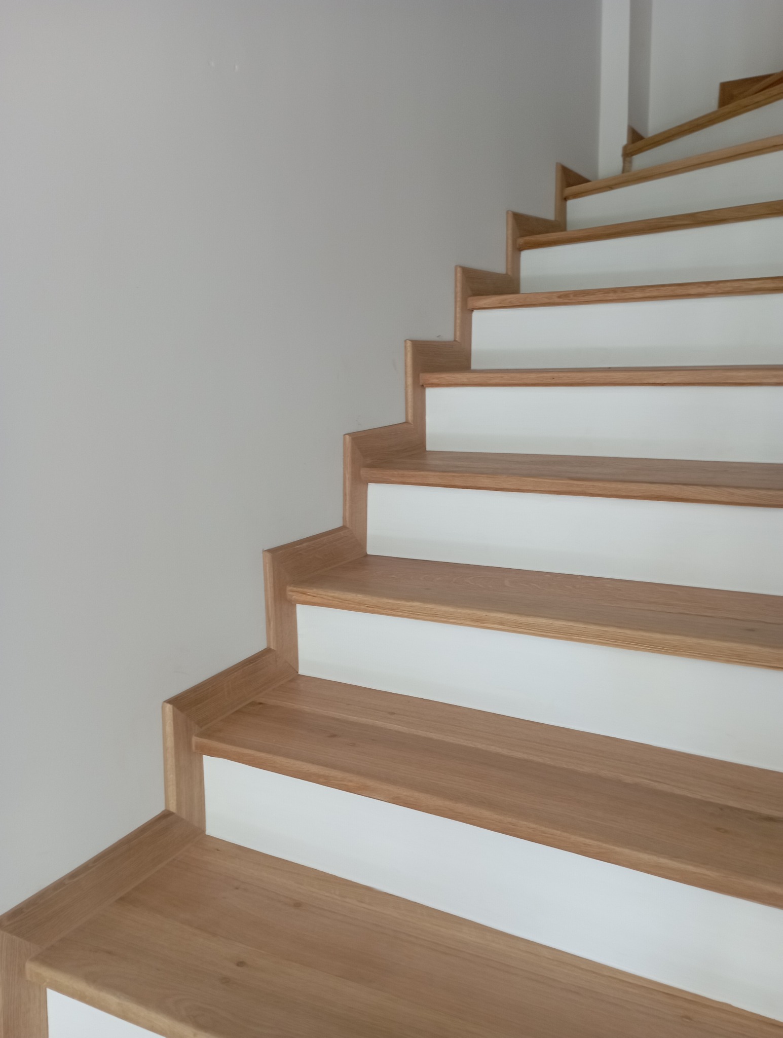 Jasne, drewniane schody z białymi podstopnicami, widok z dołu, ukazujący detale wykończenia i kąt ujęcia. Minimalistyczny design.
