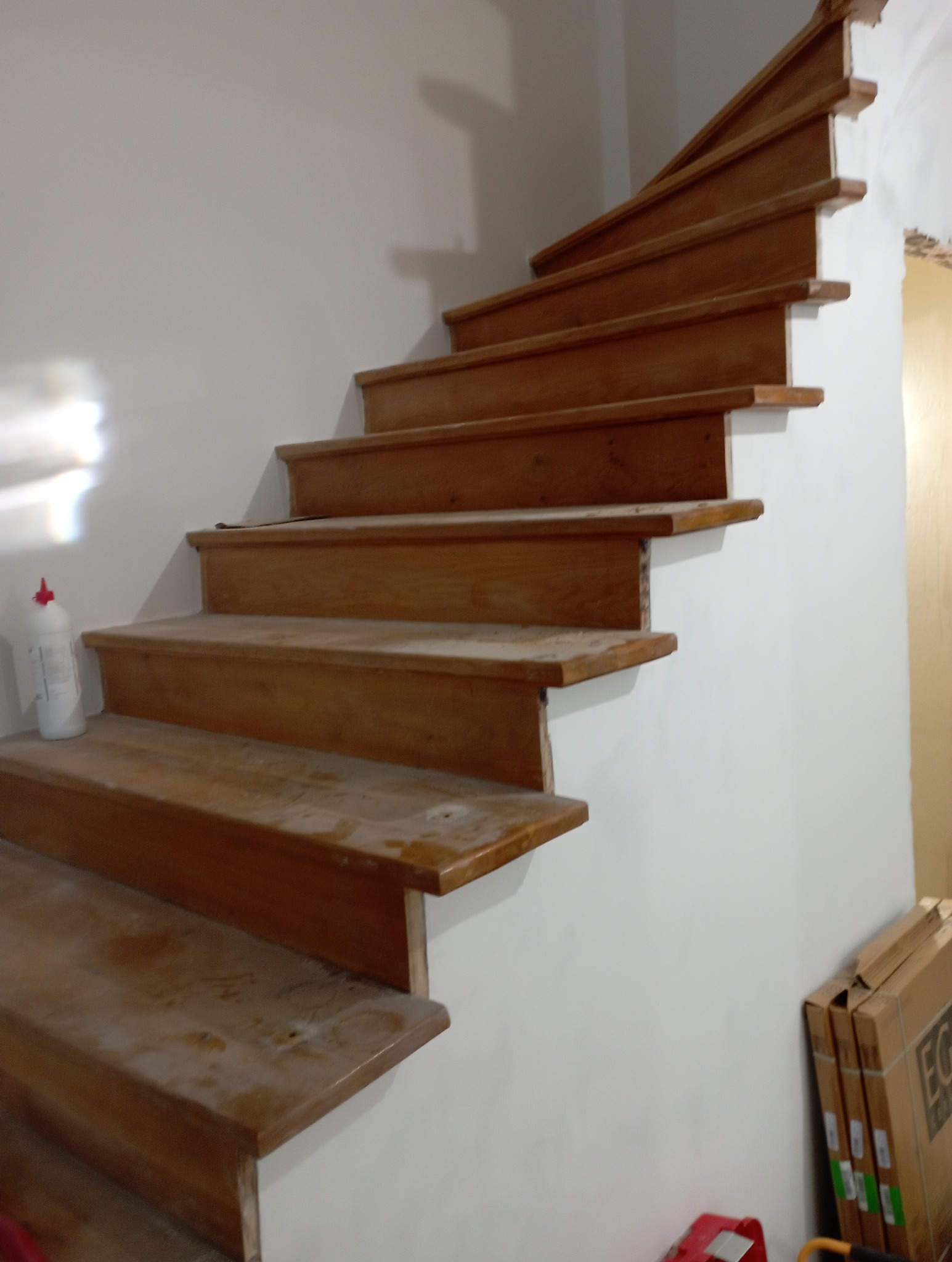 Drewniane schody po renowacji, widoczne ślady po cyklinowaniu. Na pierwszym planie butelka z preparatem do czyszczenia. Ujęcie z dołu, perspektywa podkreśla bieg schodów.