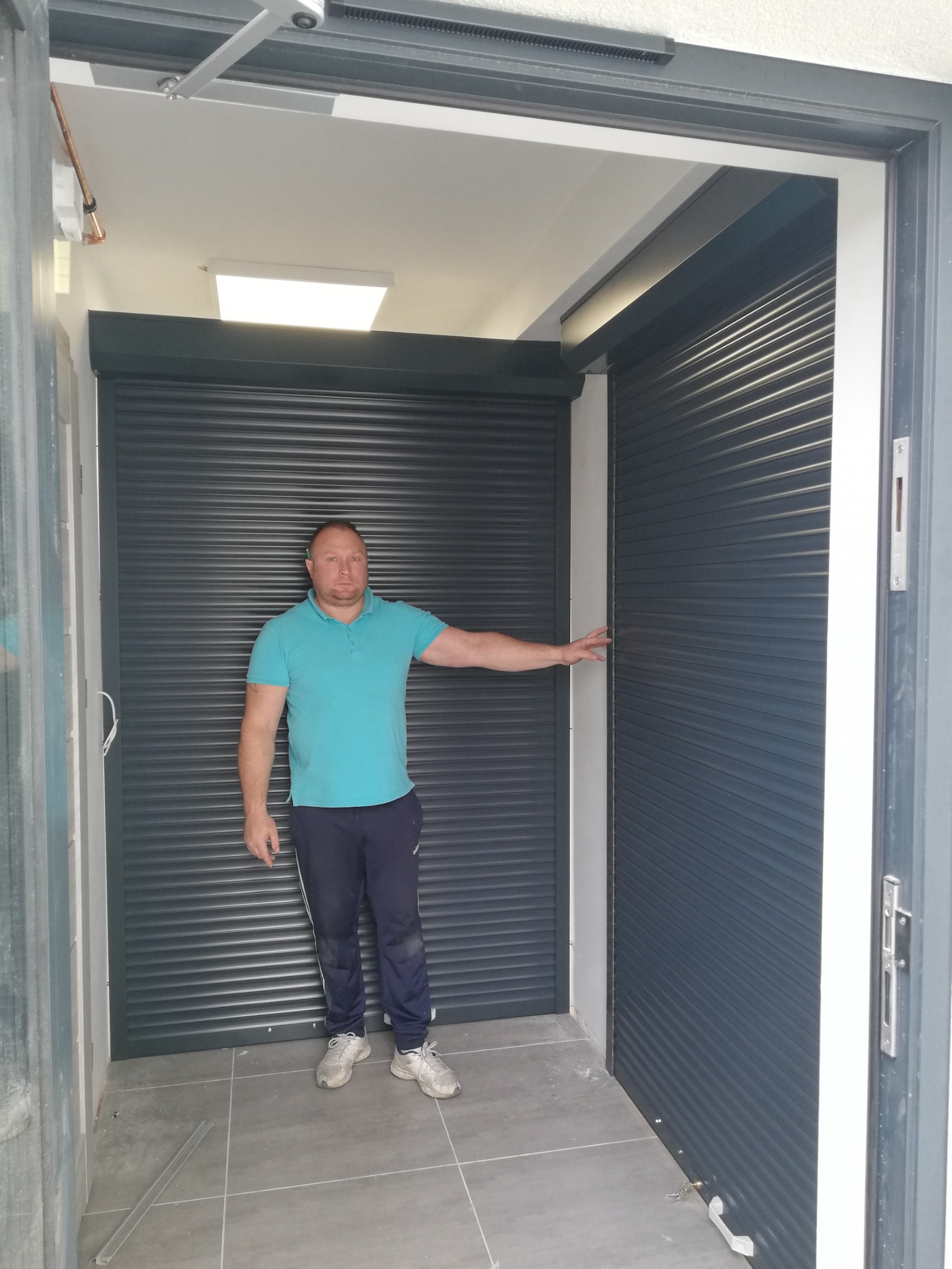 Mężczyzna prezentuje zamontowane rolety zewnętrzne w garażu, widoczne prowadnice i mechanizm otwierania.