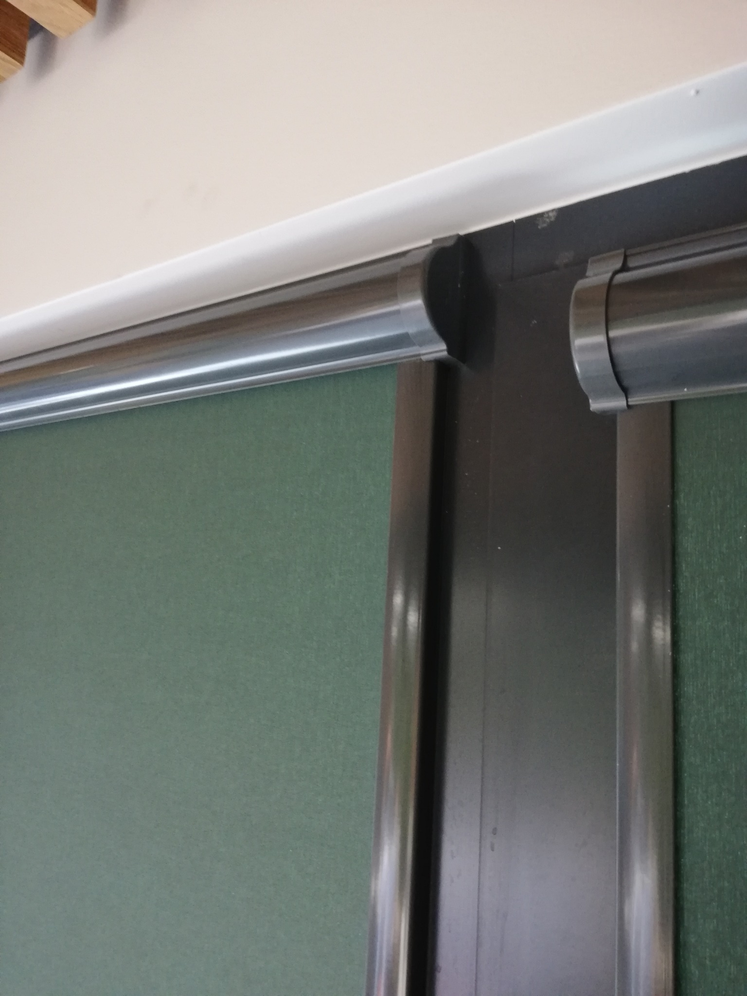 Zamknięta roleta wewnętrzna w kolorze zielonym, z widocznym mechanizmem rolety i fragmentem sufitu.
