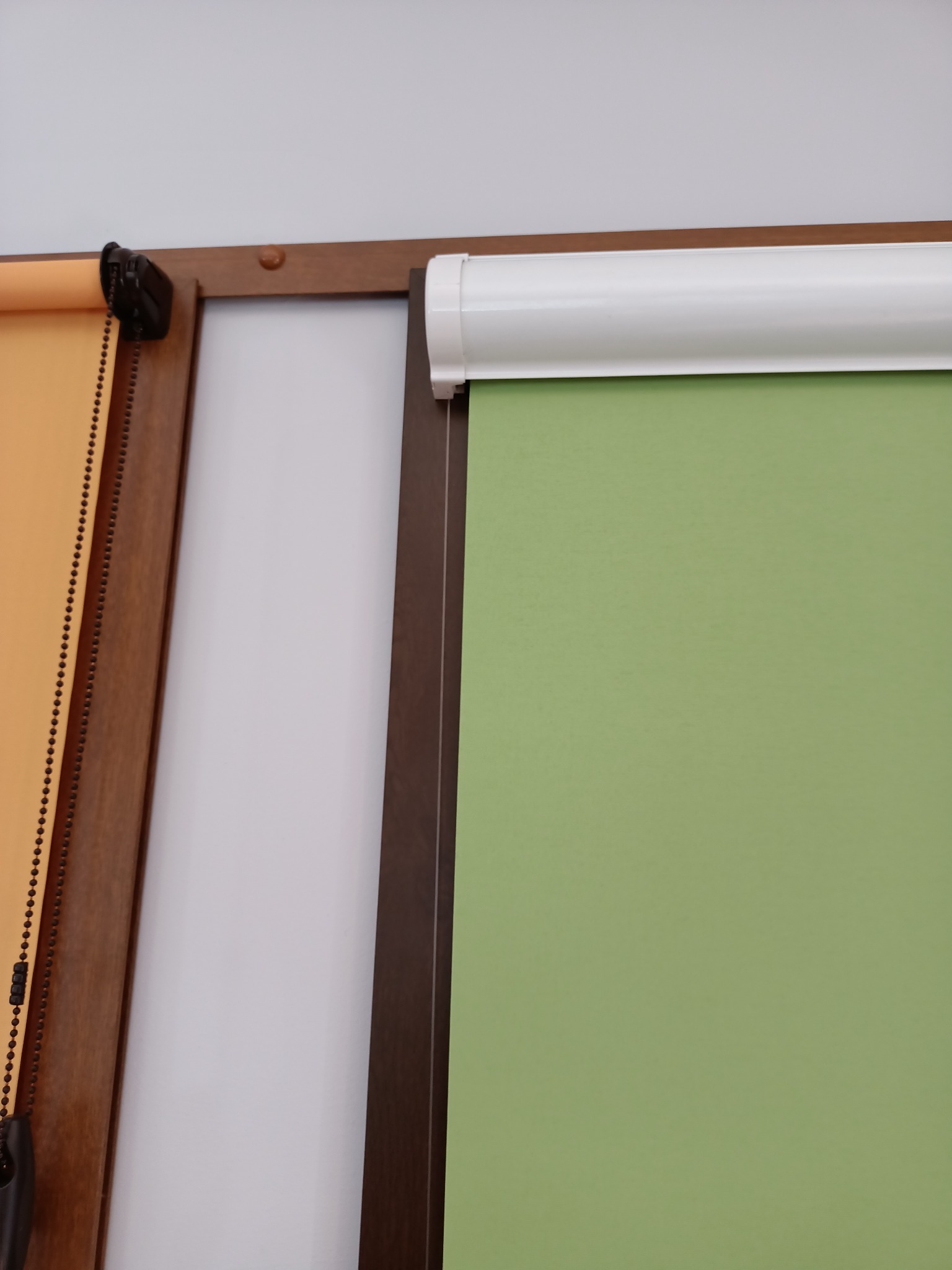 Przykładowe rolety wewnętrzne w odcieniach zieleni i beżu, z widocznymi mechanizmami łańcuszkowymi i drewnianymi ramami, prezentowane na tle białej ściany.