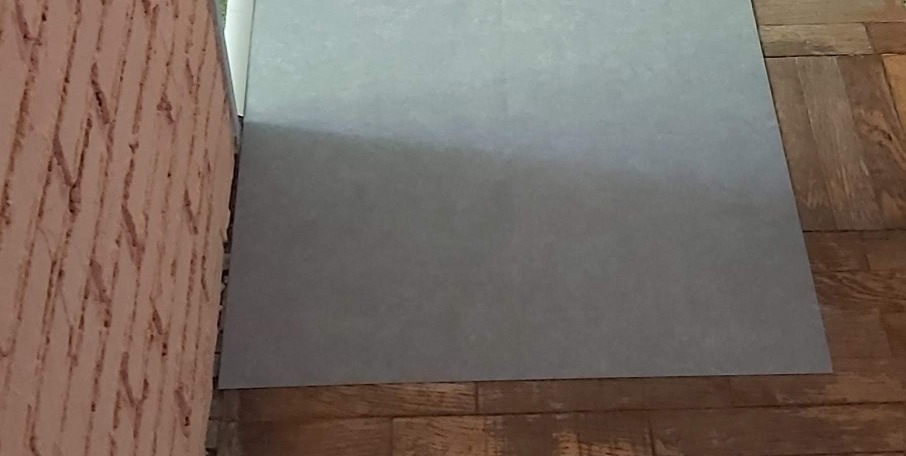 Szara płyta podłogowa częściowo ułożona na parkiecie, obok ściana z fakturą baranka.