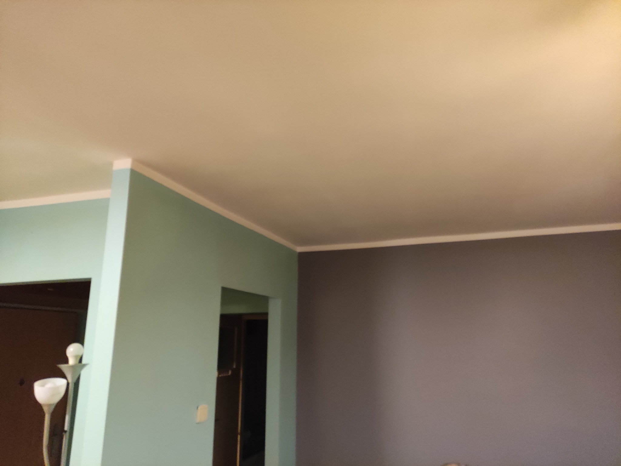 Pomieszczenie po odświeżeniu: ściany pomalowane na szaro i miętowo, biały sufit z listwami przypodłogowymi, widoczny fragment lampy.