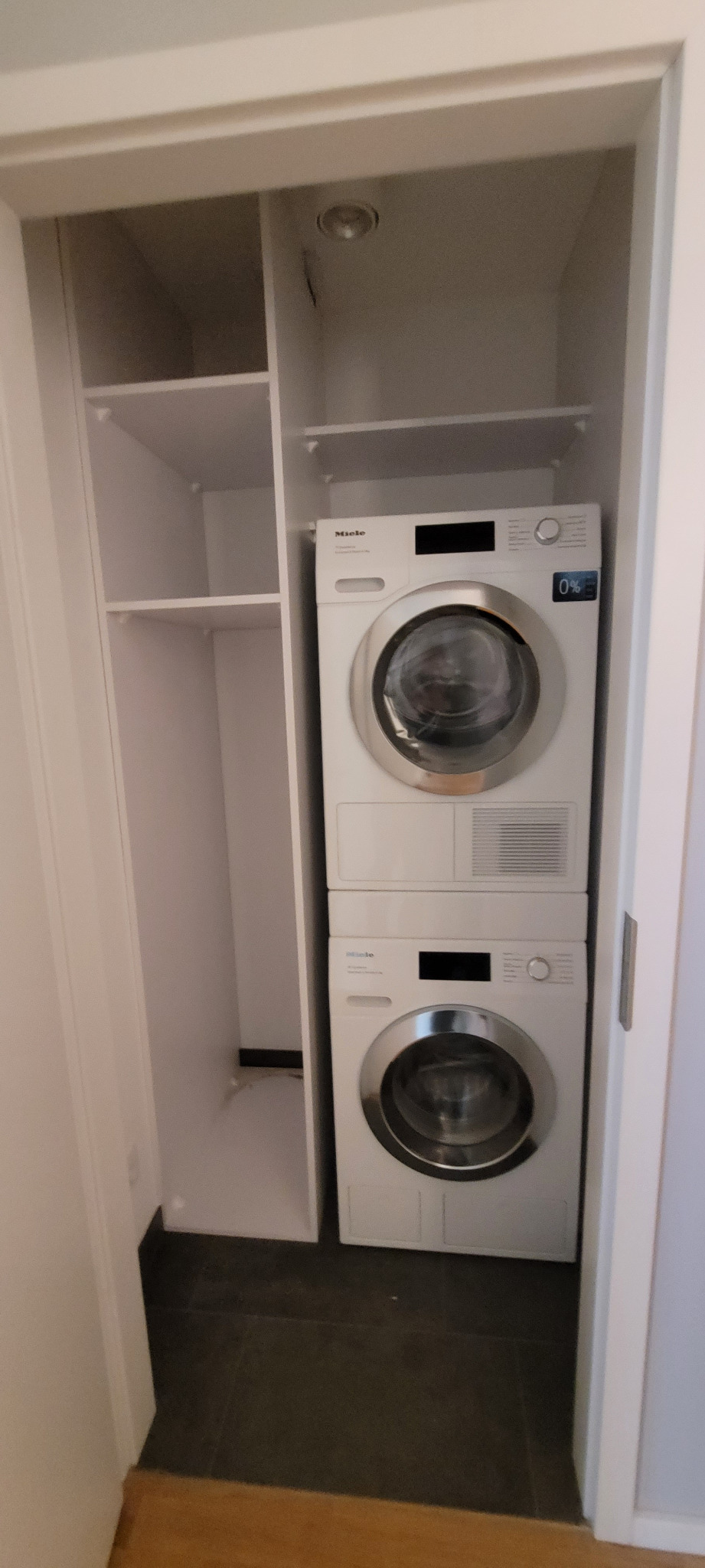 Biała szafa wnękowa z półkami i zabudowaną pralko-suszarką Miele, widok z przodu.