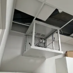 Metalowa rama serwerowa montowana pod sufitem podwieszanym, widoczne kable i otwarta przestrzeń nad sufitem.