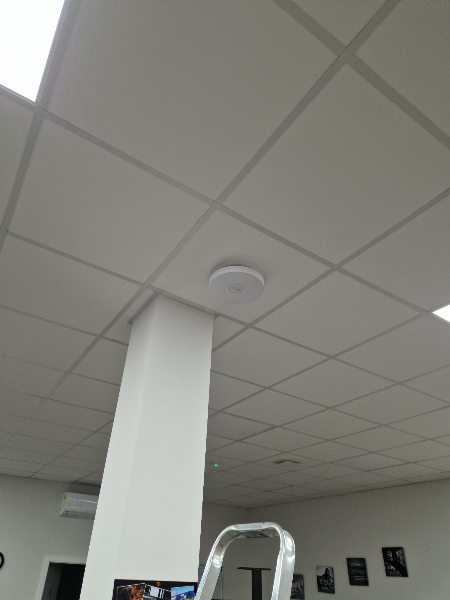Okrągły czujnik zamontowany na suficie kasetonowym w biurze w Błoniu, widoczny fragment drabiny.