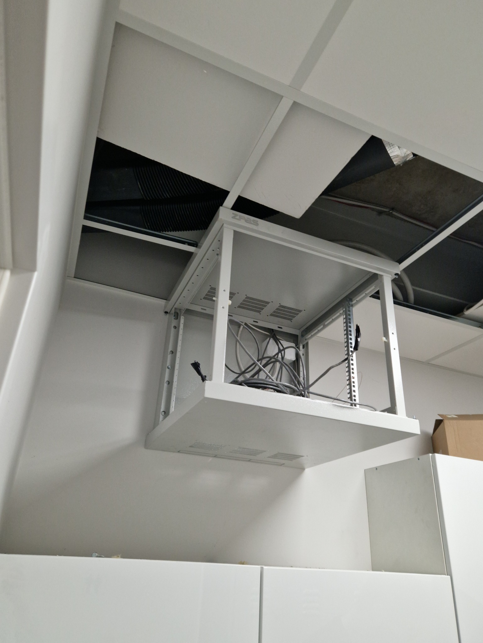 Metalowa rama serwerowa montowana pod sufitem podwieszanym, widoczne kable i otwarta przestrzeń nad sufitem.