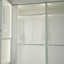 Wnętrze nowoczesnej, białej szafy wnękowej z oświetleniem LED, widoczne półki i drążki na ubrania.