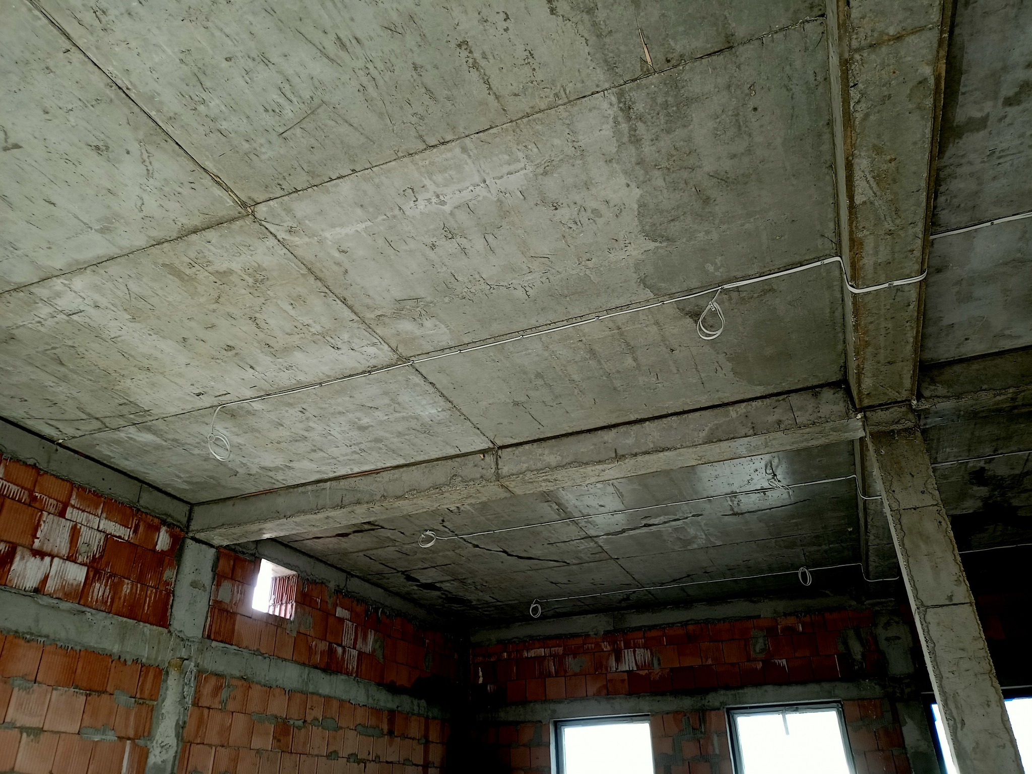Surowy betonowy strop z widocznymi przewodami elektrycznymi w nowo powstającym budynku z czerwonej cegły.