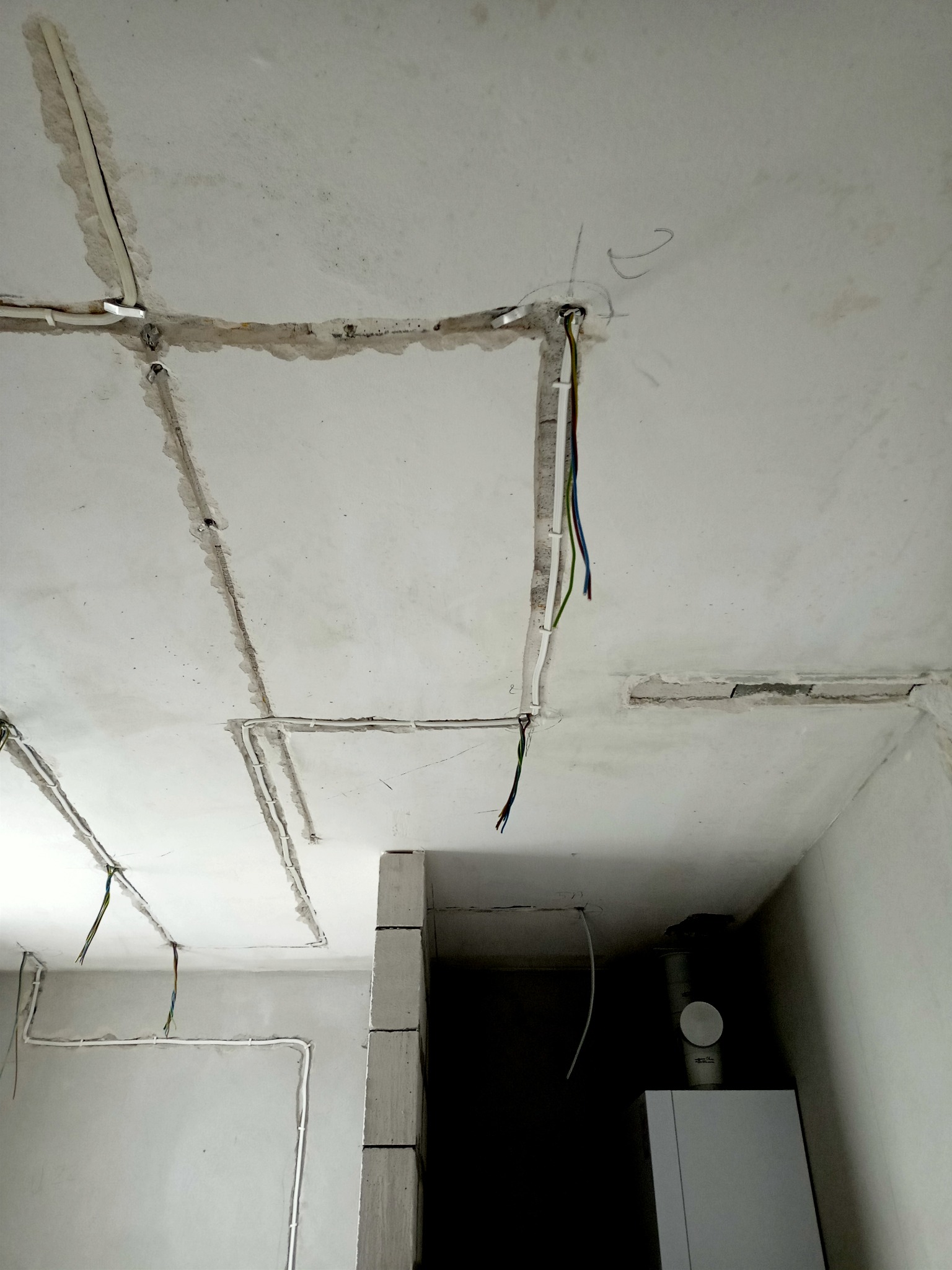 Instalacja elektryczna w bruzdach na suficie i ścianie, widoczne przewody i puszki, w tle biały bojler.
