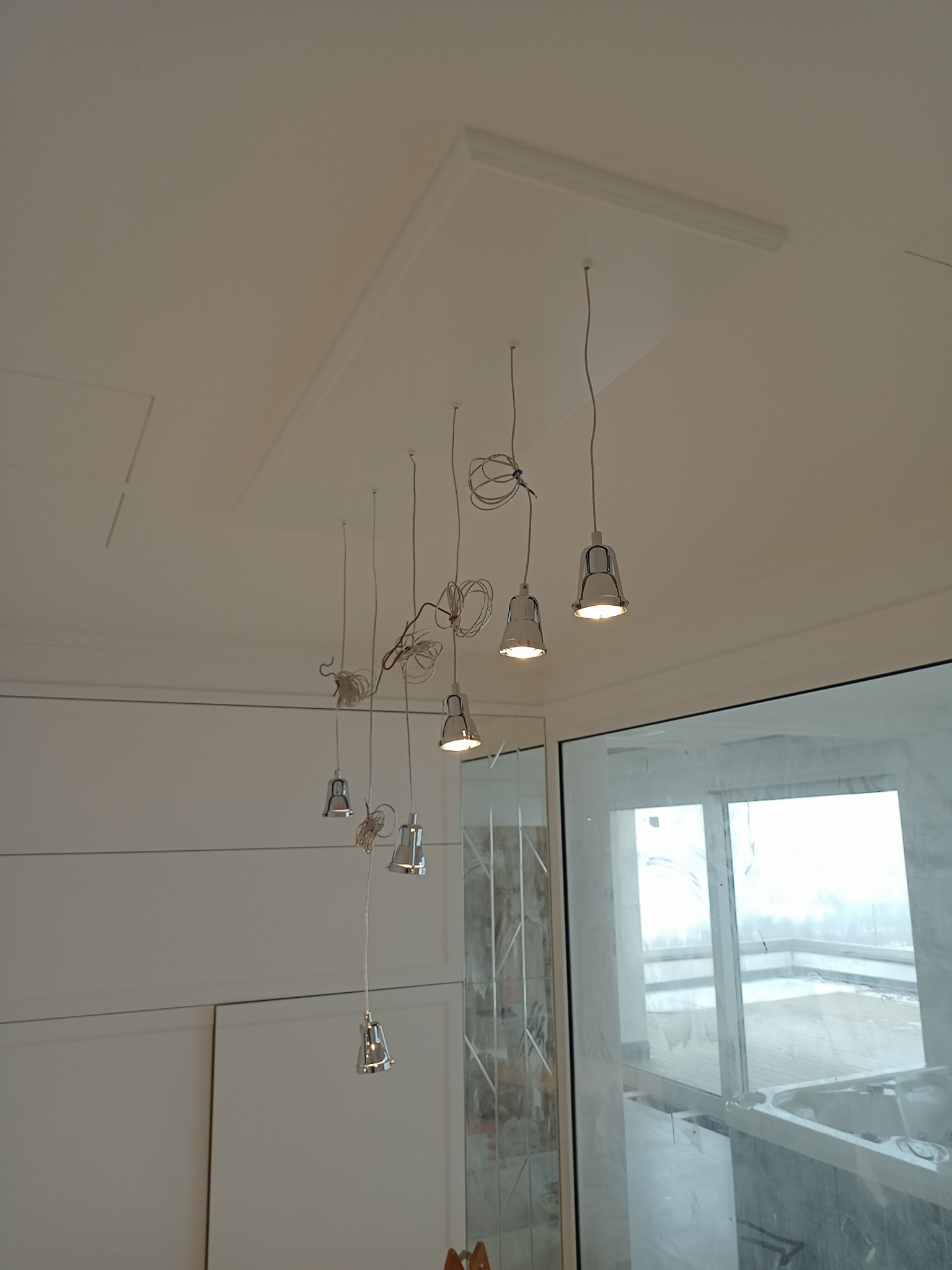 Montaż wiszących lamp sufitowych z chromowanymi kloszami w nowoczesnym wnętrzu, widoczne kable i elementy mocujące przed ostatecznym wykończeniem.