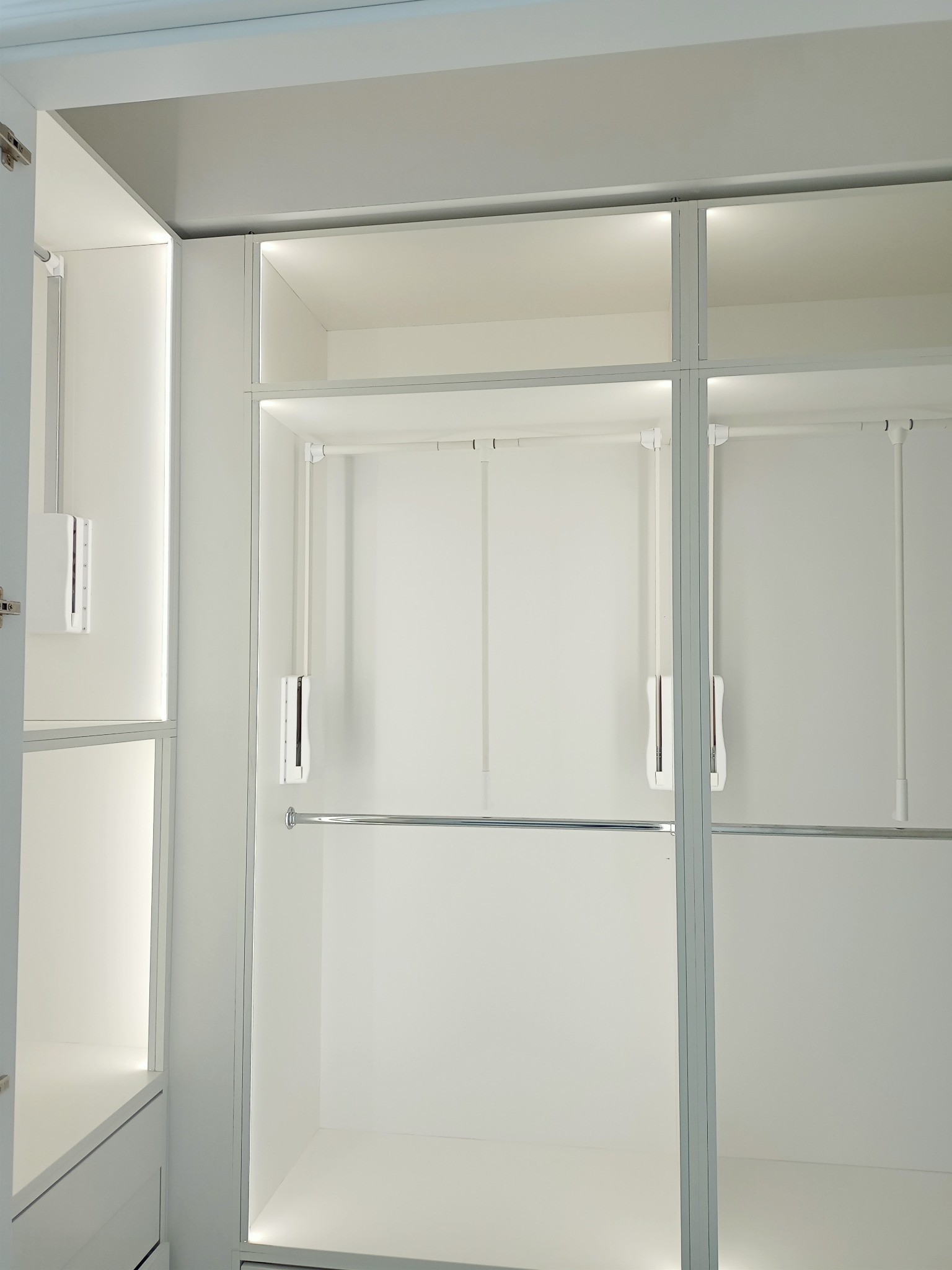 Wnętrze nowoczesnej, białej szafy wnękowej z oświetleniem LED, widoczne półki i drążki na ubrania.