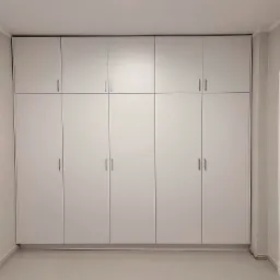 Biała zabudowa meblowa od podłogi do sufitu z minimalistycznymi uchwytami, dopasowana do koloru ścian, z widoczną białą stolarką drzwiową po prawej stronie.