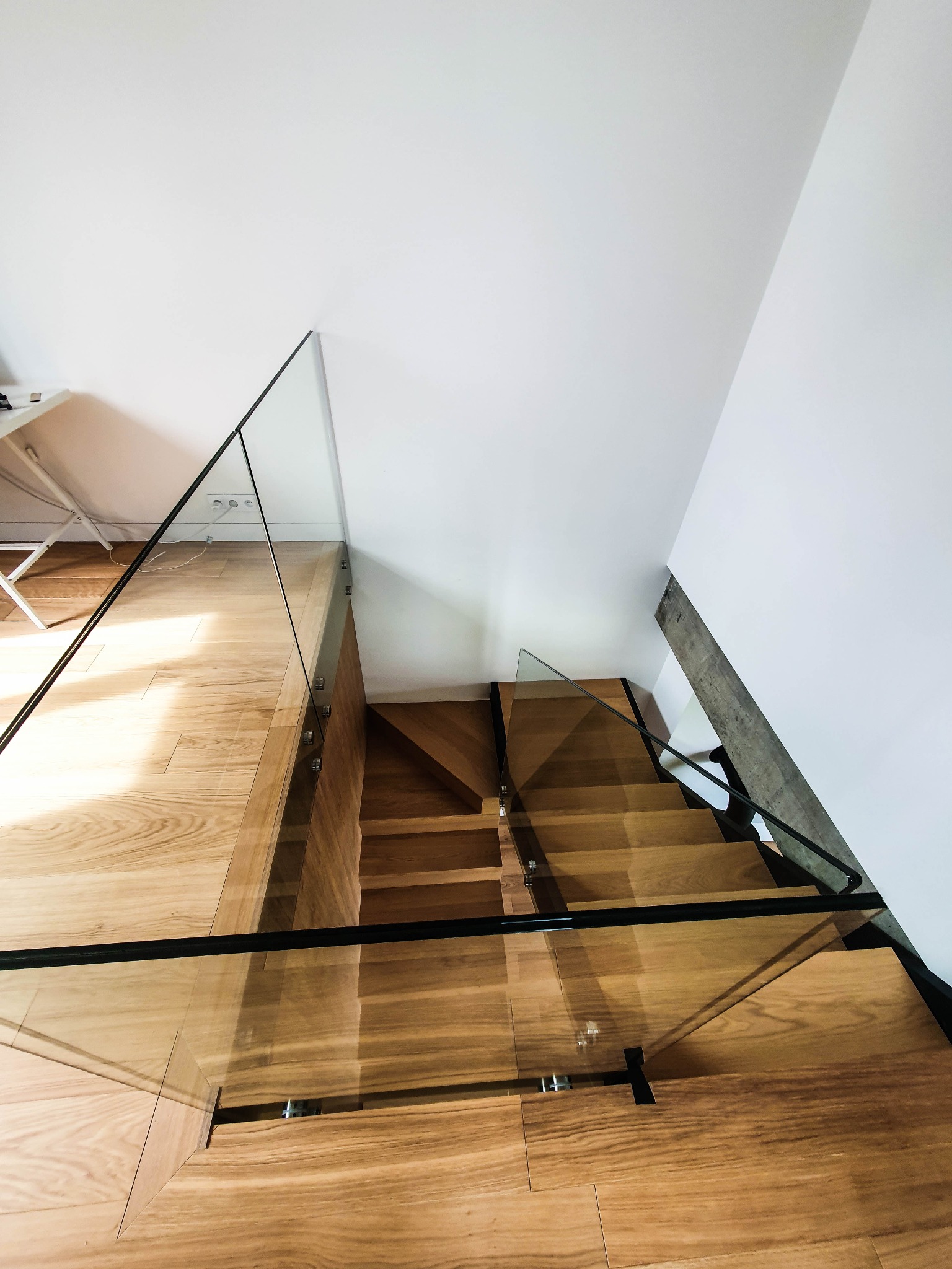 Nowoczesne schody drewniane z balustradą szklaną i czarną poręczą, widok z góry, minimalistyczne wnętrze.