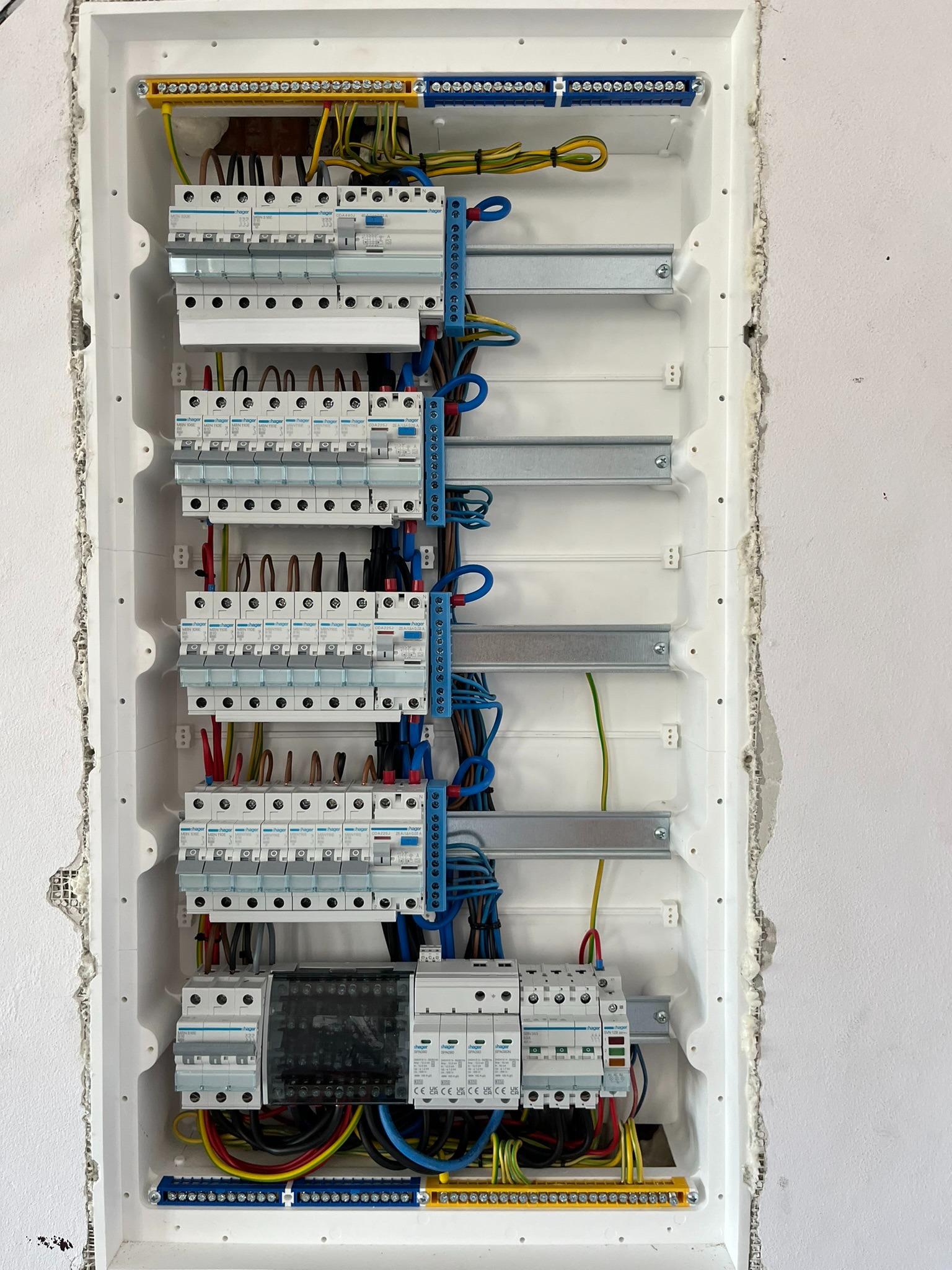 Zamknięta skrzynka elektryczna z zainstalowanymi bezpiecznikami i okablowaniem w białej obudowie, zamontowana we wnęce ściany z surowym wykończeniem.