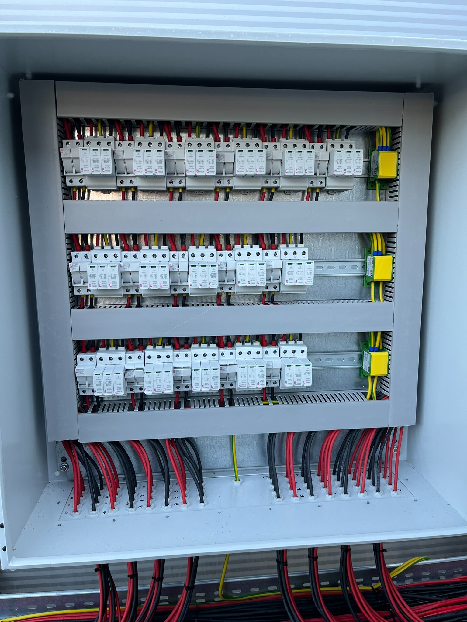 Rozdzielnica elektryczna z zabezpieczeniami przepięciowymi, kable w kolorach czarnym, czerwonym i żółto-zielonym. Estetyczne wykonanie instalacji.