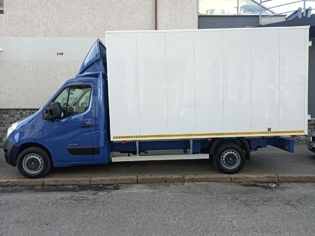 Niebieski samochód dostawczy Renault Master z białą zabudową kontenerową, zaparkowany na chodniku przed budynkiem.