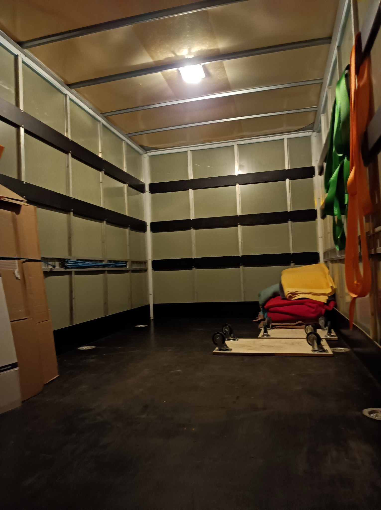 Wnętrze przestrzeni ładunkowej samochodu dostawczego z zabezpieczeniami, pasami transportowymi i platformami na kółkach, przygotowane do załadunku mebli i sprzętów.