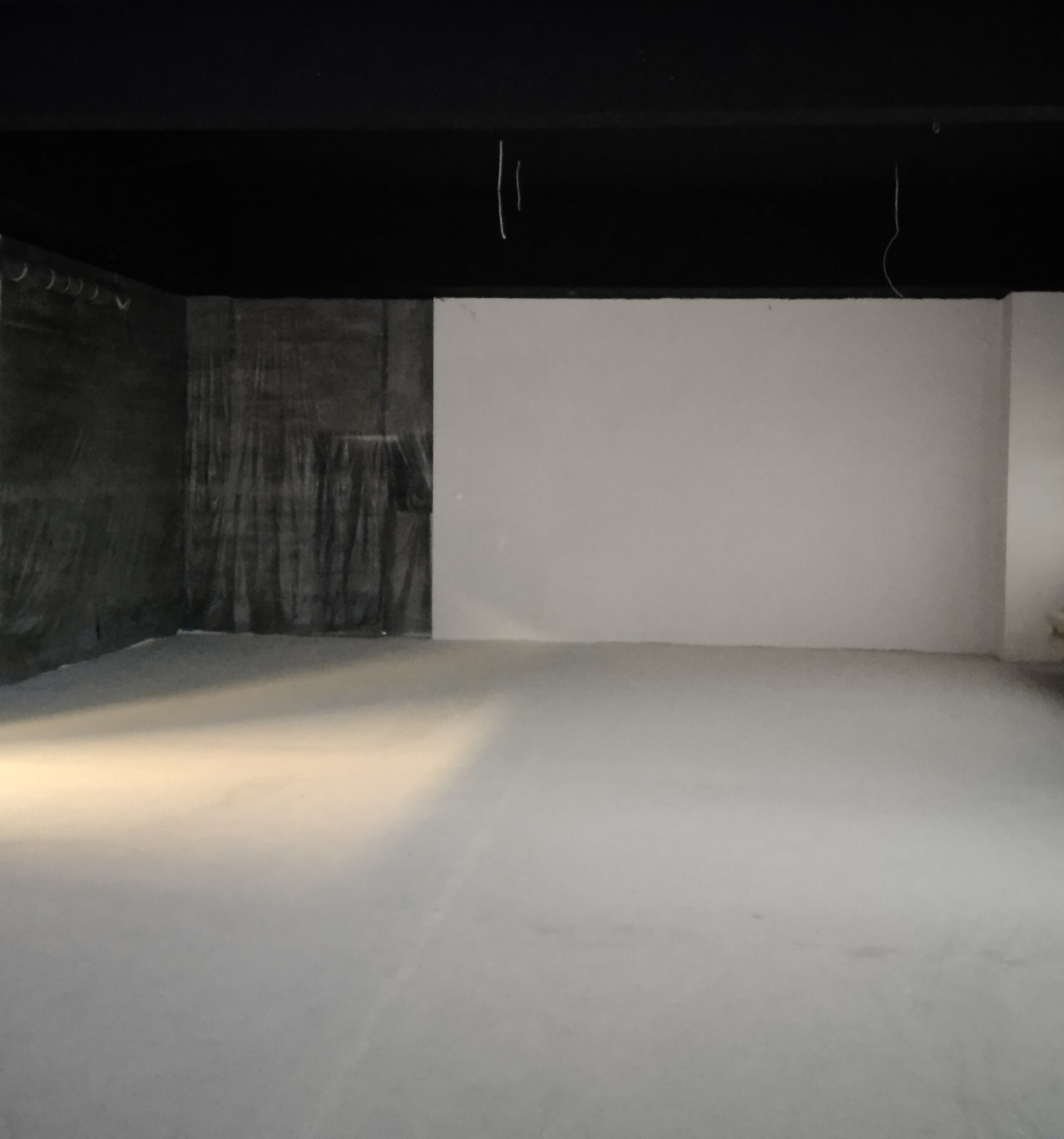 Przygotowane do prac wykończeniowych wnętrze: zabezpieczona folią ściana, surowa podłoga, biała ściana, wiszące kable.