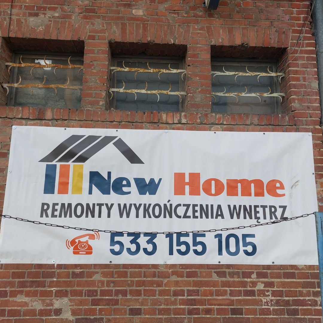Baner reklamowy firmy 'New Home' z numerem telefonu, wiszący na starej, ceglanej ścianie z trzema oknami zabezpieczonymi metalowymi kratami.