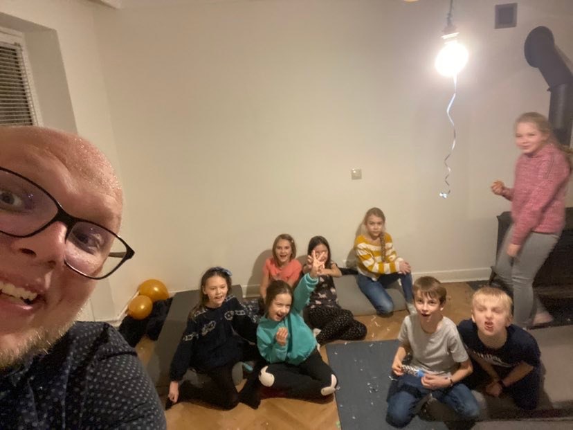 Selfie iluzjonisty z grupą dzieci po występie, widoczne balony i konfetti na podłodze, uśmiechnięte twarze dzieci i iluzjonisty.