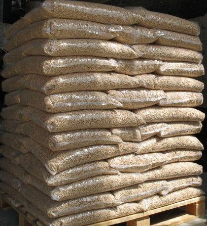 Stos palet z workami pelletu drzewnego, ułożonych warstwami na drewnianej palecie, widoczne przezroczyste worki.