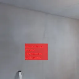 Świeżo otynkowana ściana w jasnym odcieniu szarości, widoczna faktura tynku, narożnik okna w prawym górnym rogu kadru, u dołu fragment narzędzia malarskiego.