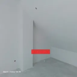 Surowe wykończenie wnętrza poddasza, ściany i sufit po szpachlowaniu, widoczne gniazdko elektryczne w ścianie, podłoga wylewka, niezagruntowana.