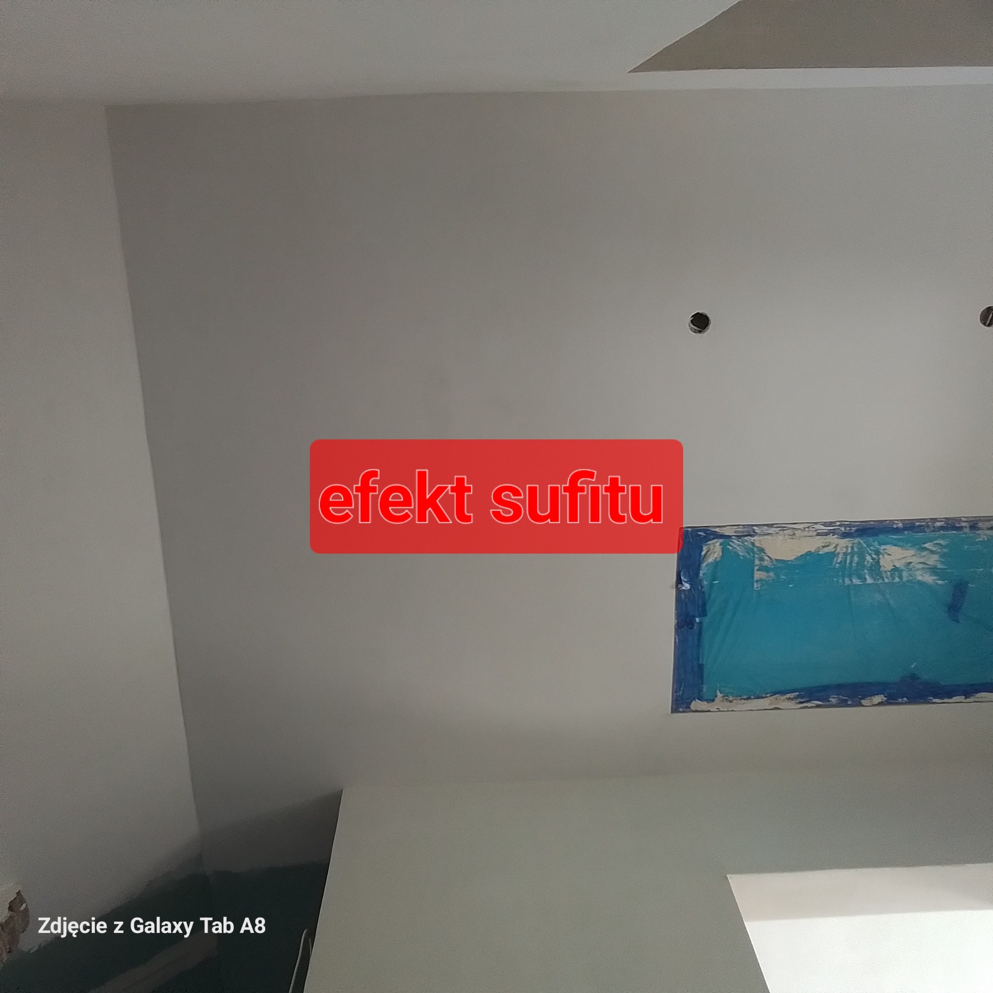 Biały sufit po szpachlowaniu i malowaniu, z widocznymi otworami na oświetlenie i zabezpieczonym fragmentem taśmą malarską.