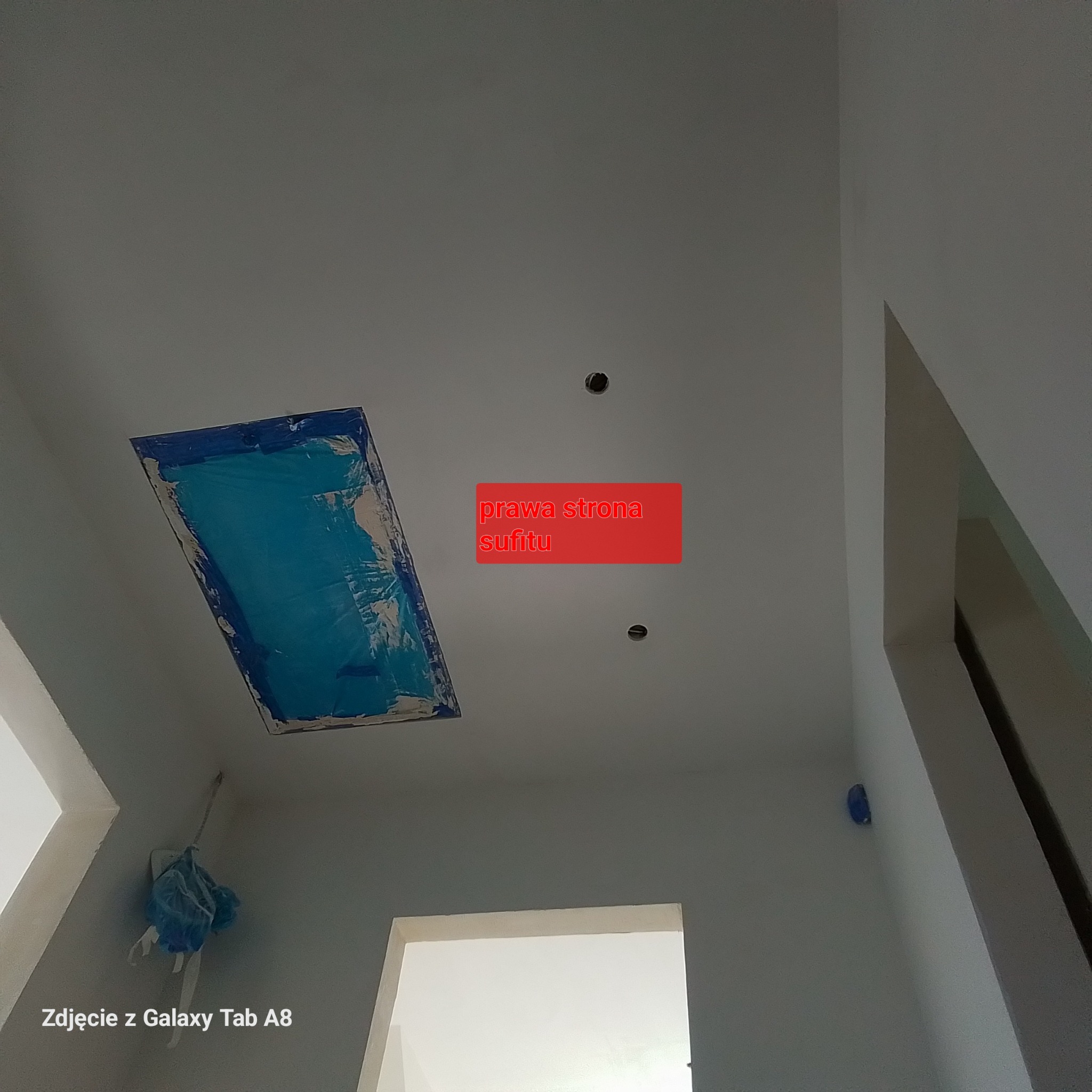 Przygotowanie otworu w suficie, zabezpieczonego niebieską folią malarską, przed dalszymi pracami wykończeniowymi. Widoczne otwory na oświetlenie.