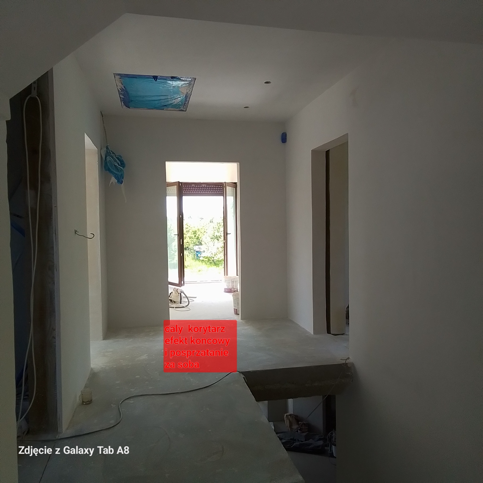 Korytarz po pracach wykończeniowych, ściany i sufit pomalowane na biało, zabezpieczona folią lampa w suficie, widoczne drzwi balkonowe i elementy instalacji elektrycznej.