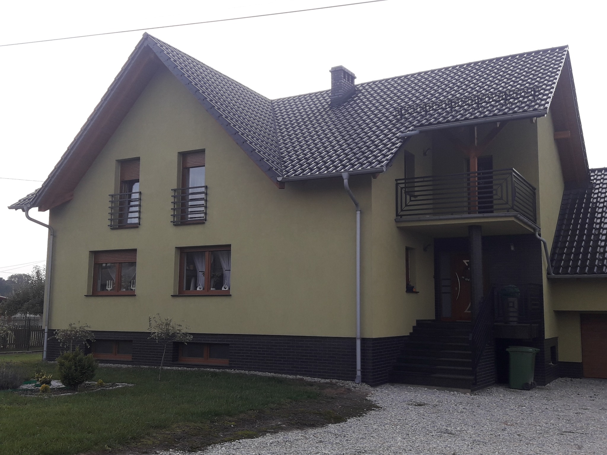 Dom jednorodzinny z ciemną dachówką karpiówką, widoczne rynny, obróbki blacharskie i fragment elewacji.