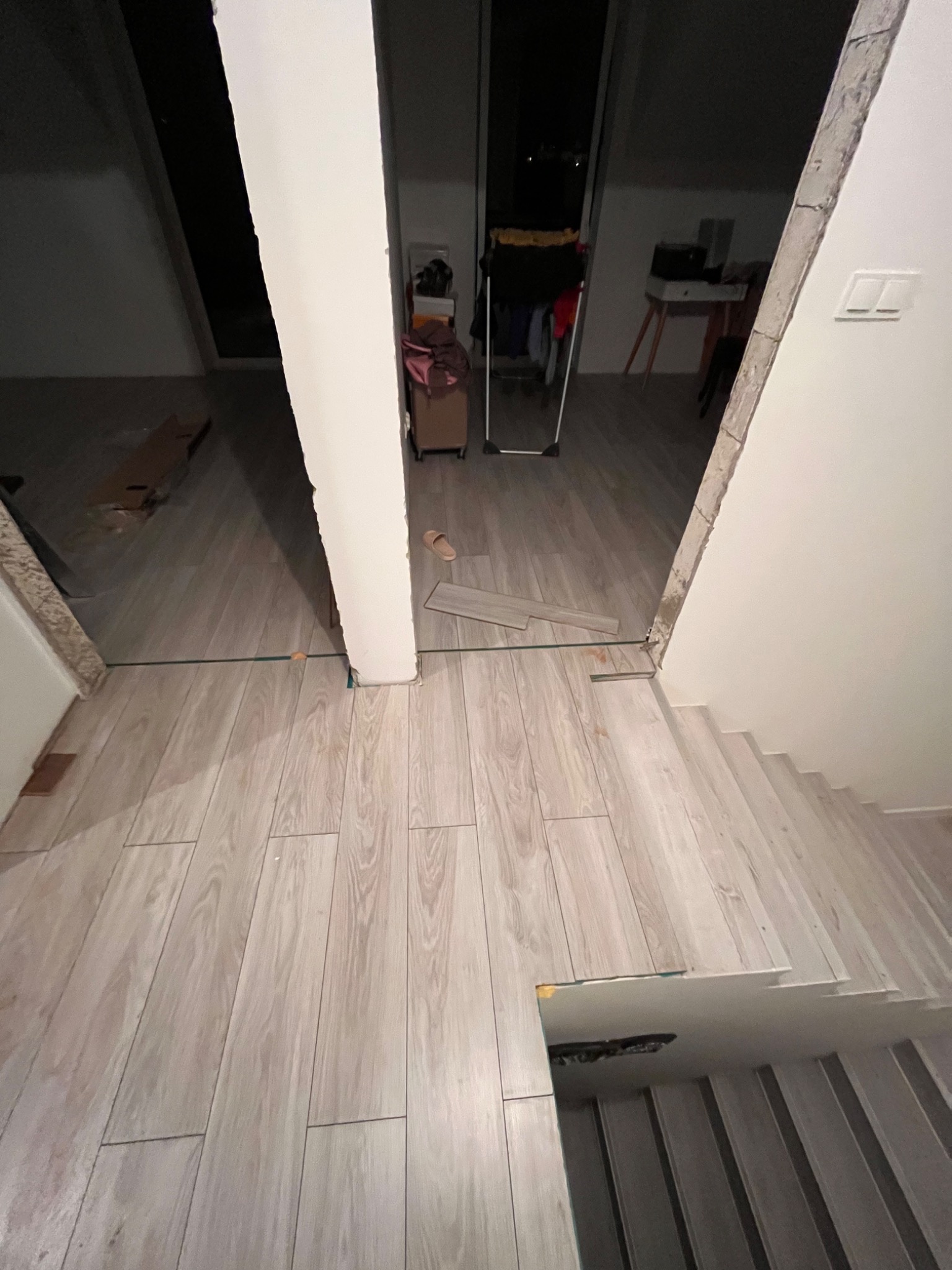 Układanie jasnych paneli podłogowych imitujących drewno, widoczne niedokończone fragmenty przy schodach i filarze, listwy przypodłogowe jeszcze nie zamontowane.