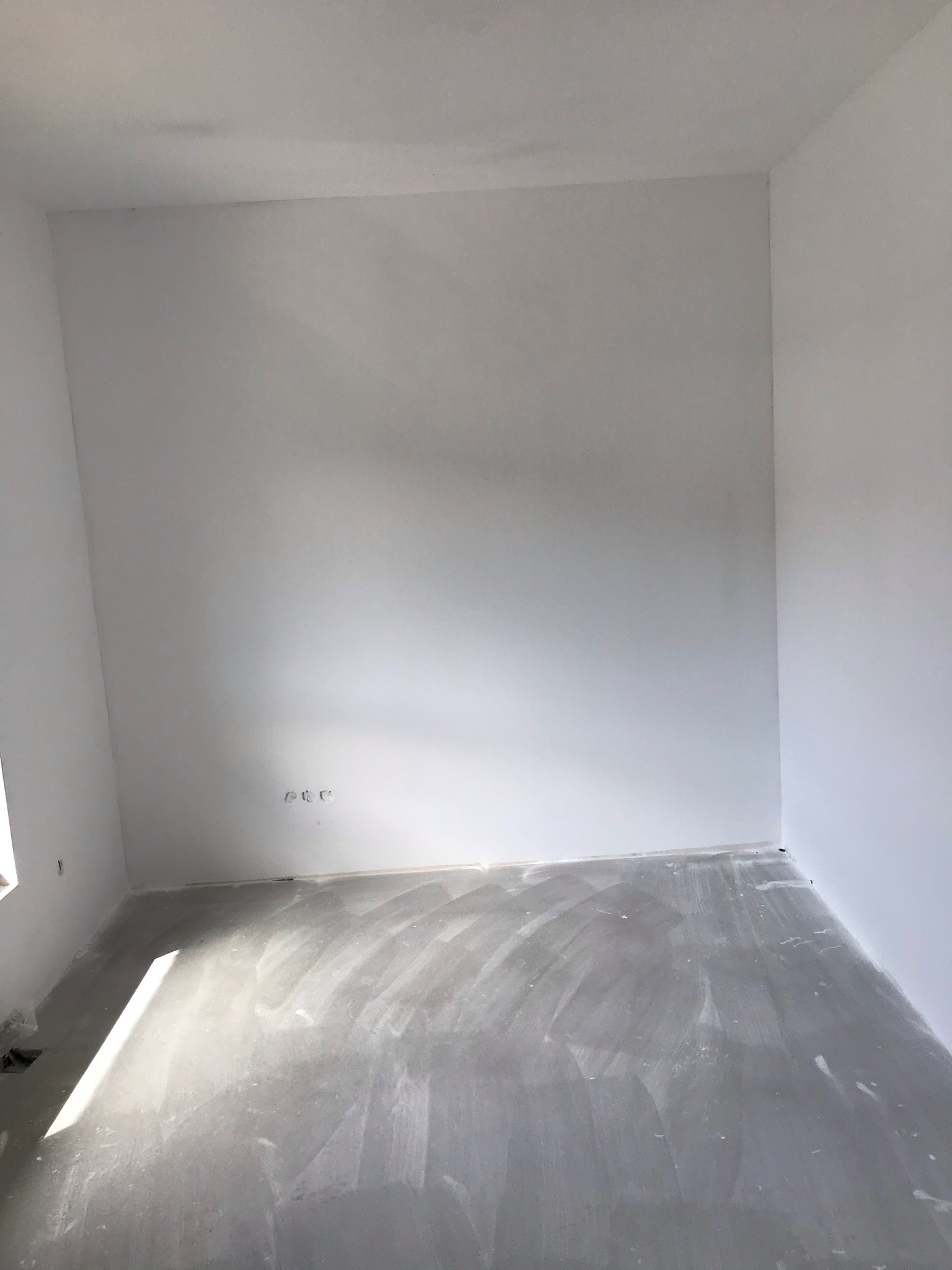 Pokój po nałożeniu gładzi, ściany i podłoga pokryte szarą warstwą, widoczne puszki elektryczne w ścianie.