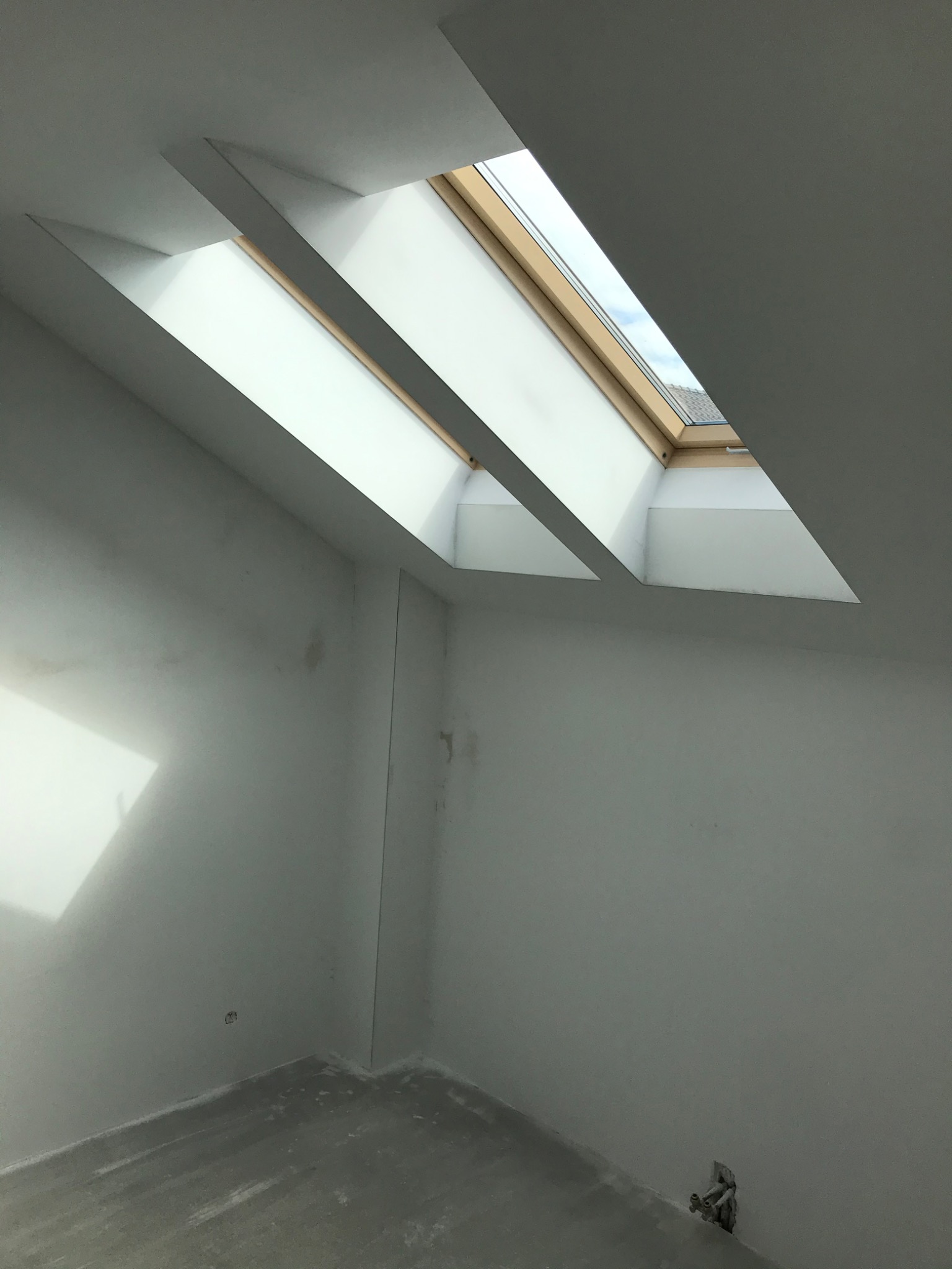 Poddasze z oknem dachowym po wykonaniu gładzi, widoczne ślady szlifowania na ścianach i podłodze, przygotowane do malowania.
