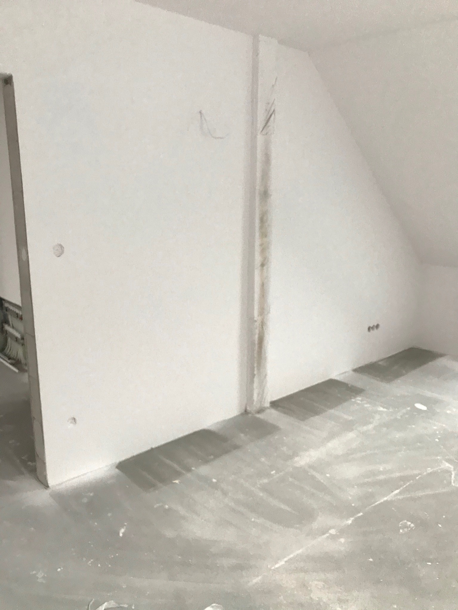 Poddasze w trakcie prac wykończeniowych: widoczne ściany z płyt karton-gips, szpachlowane łączenia, przygotowany betonowy podkład podłogowy, instalacja elektryczna w ścianie.