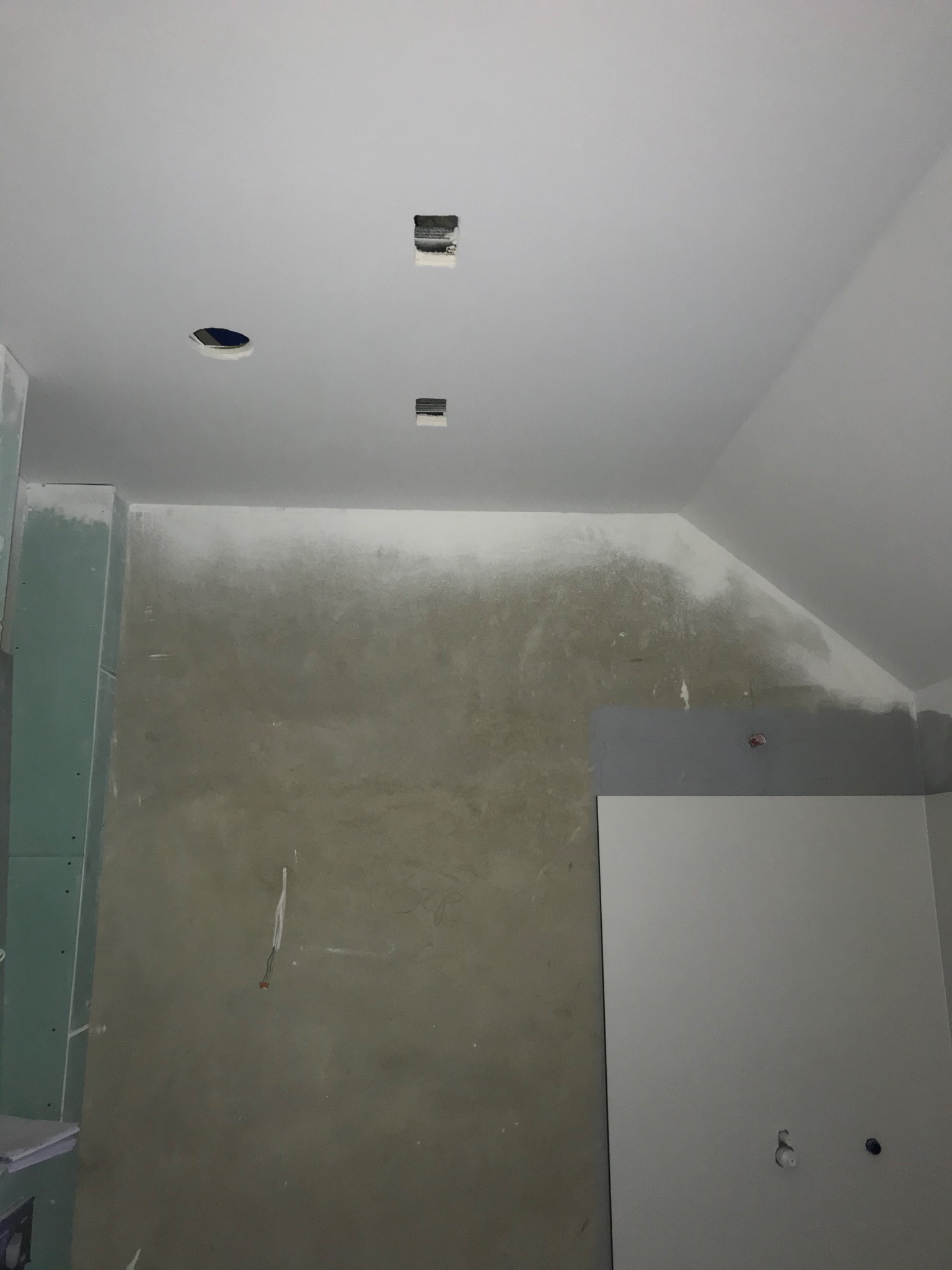 Wnętrze w trakcie prac: ściana po nałożeniu pierwszej warstwy gładzi, widoczne płyty karton-gips na ścianie bocznej, otwory w suficie przygotowane pod oświetlenie.