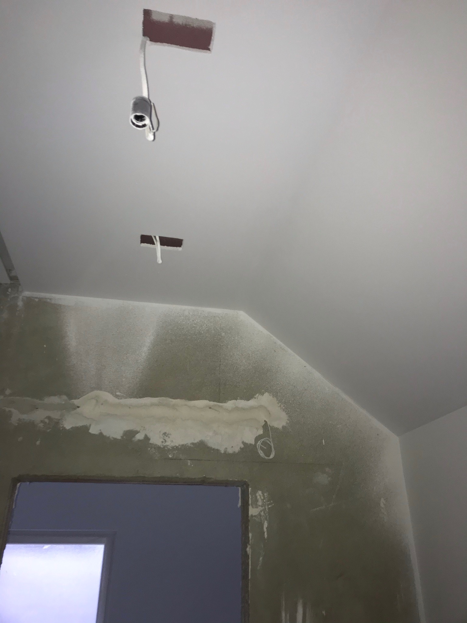 Wnętrze w trakcie prac remontowych: ściana z widocznymi śladami po gładzi, otwór drzwiowy, wystające kable z sufitu, przygotowanie do wykończenia.