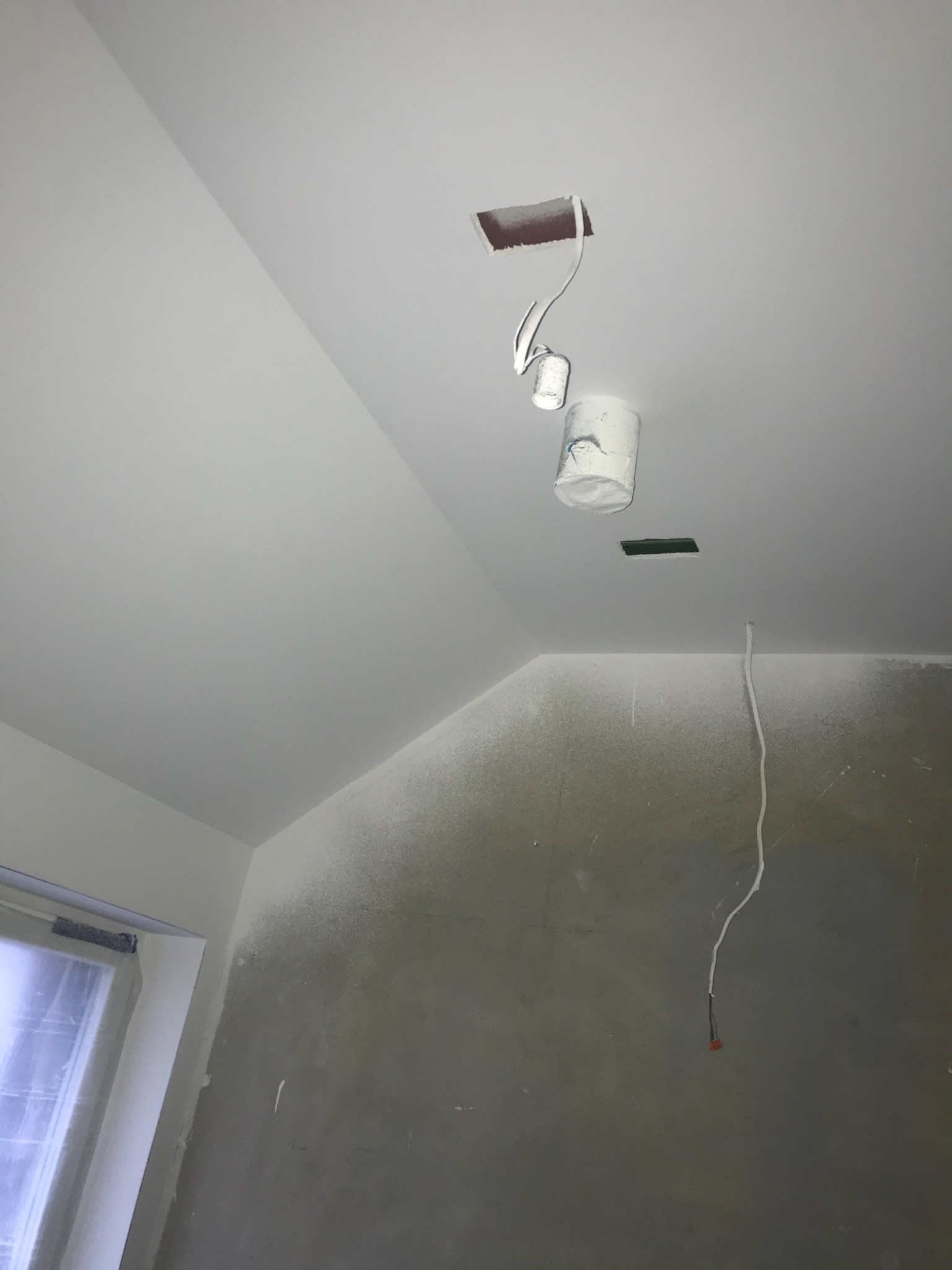 Świeżo pomalowany, biały sufit z widocznym otworem na oświetlenie, wiszącą puszką po farbie i wystającym przewodem elektrycznym; ściana w szarym kolorze w trakcie prac wykończeniowych.