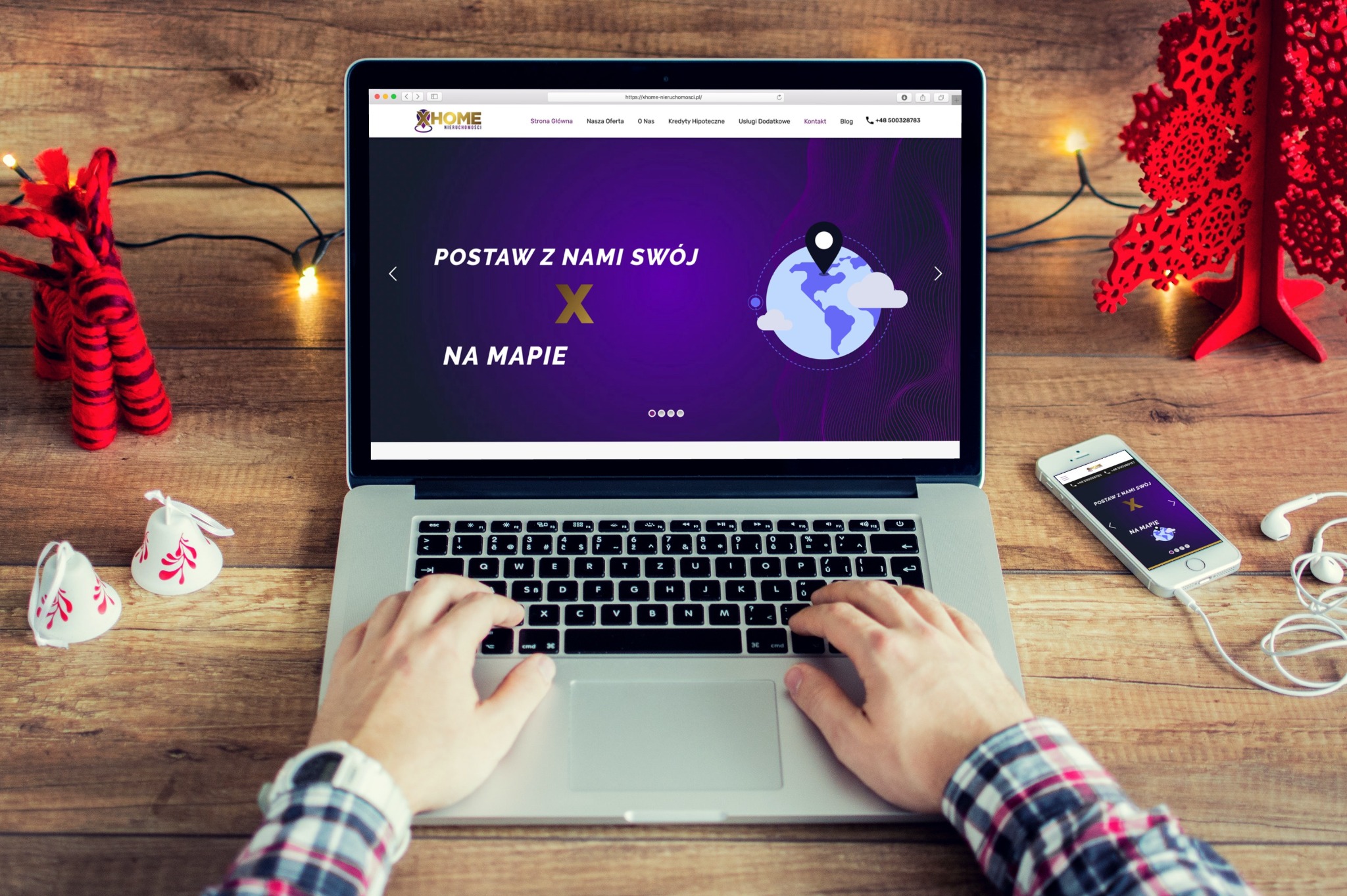 Osoba pisze na laptopie prezentującym stronę internetową firmy XHOME Nieruchomości z hasłem 'Postaw z nami swój X na mapie', obok leży telefon z wyświetloną tą samą stroną, słuchawki,...