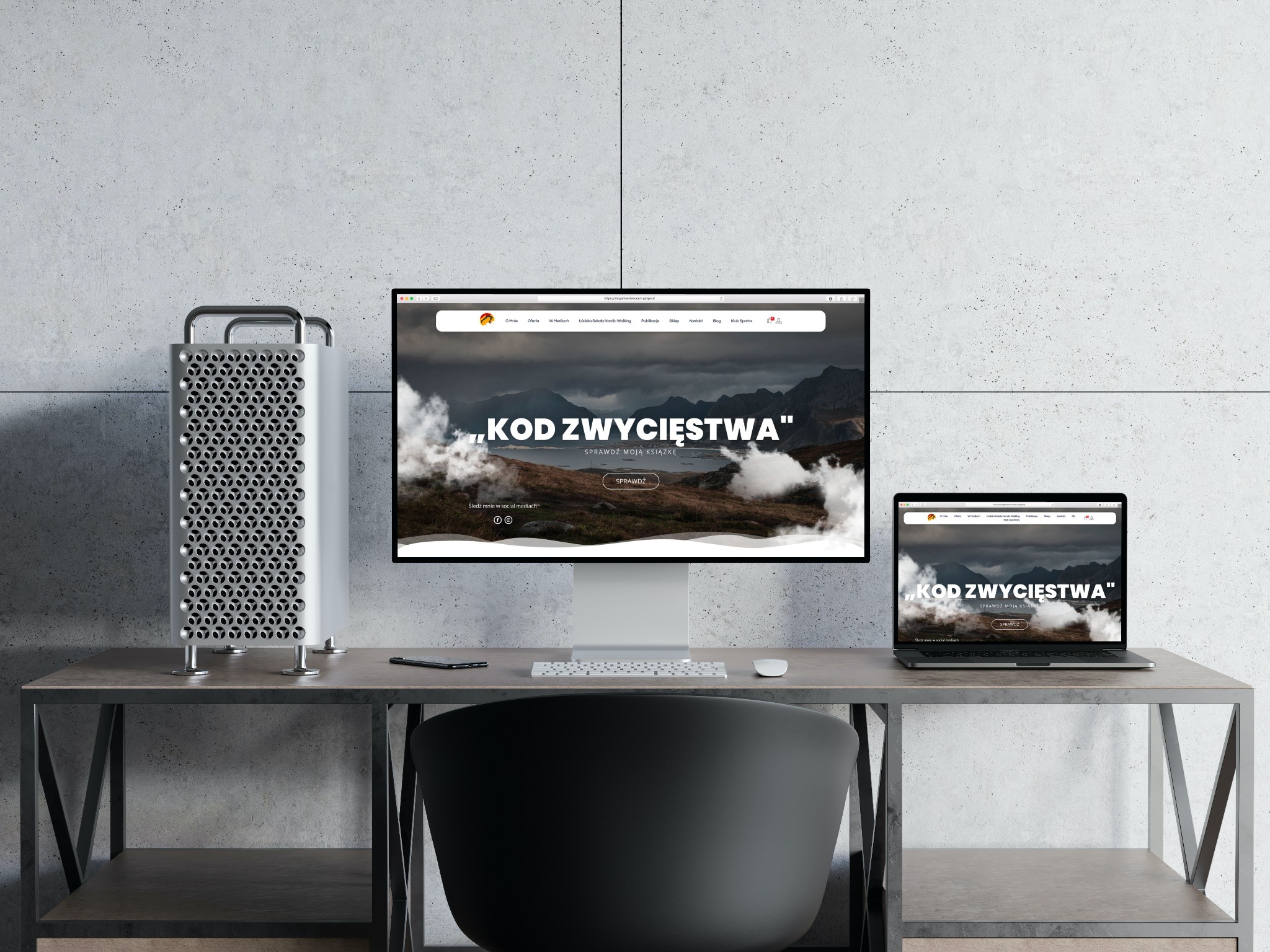 Stanowisko pracy z komputerem stacjonarnym i laptopem, na których wyświetlona jest strona internetowa z nagłówkiem 'KOD ZWYCIĘSTWA' i motywem górskim. Minimalistyczne biurko z szarą ścianą w tle.