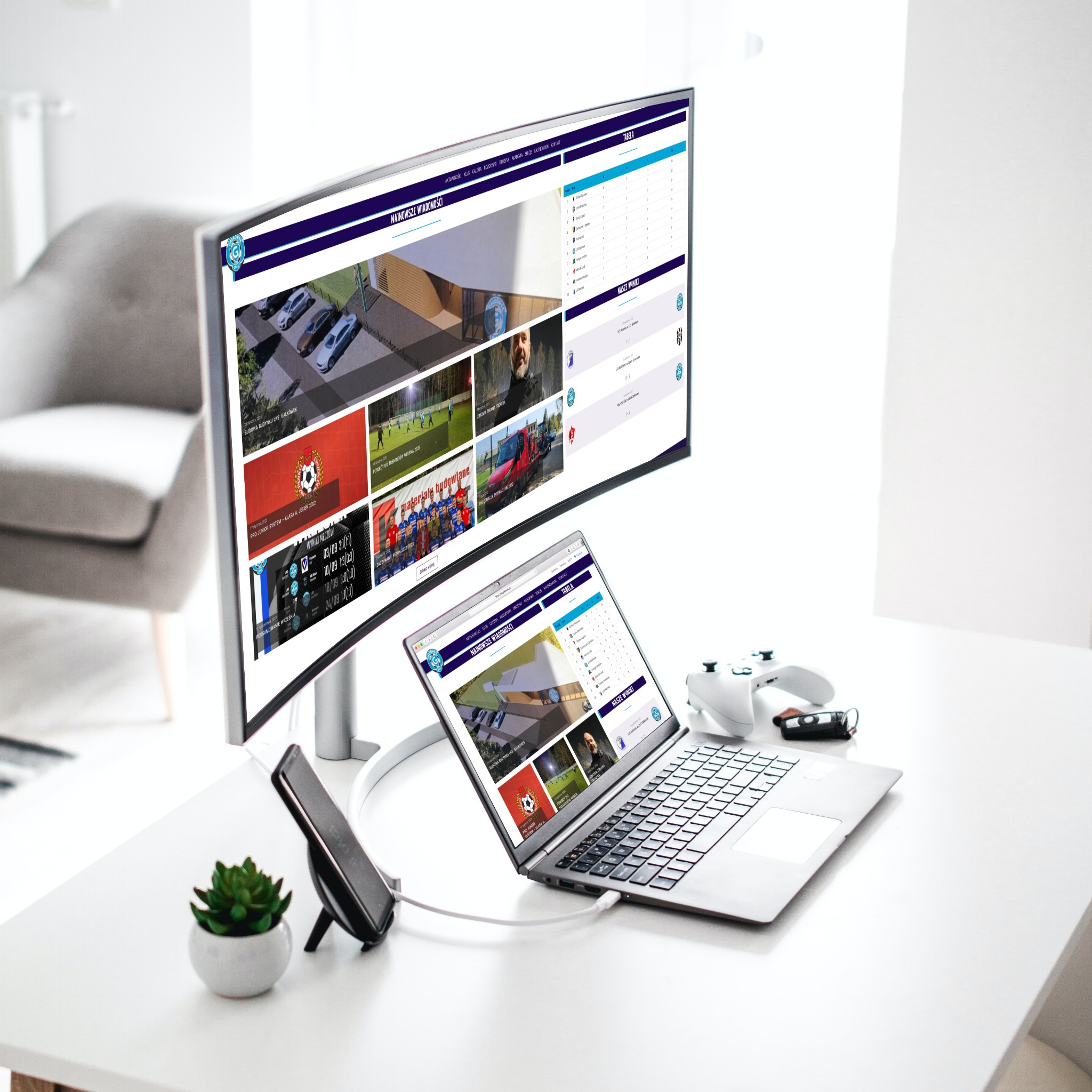 Stanowisko pracy z monitorem ultrapanoramicznym i laptopem wyświetlającymi stronę internetową klubu sportowego z aktualnościami, tabelą wyników i zdjęciami, obok kontroler do gier i roślina...