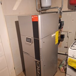 Dział EcoTerm firmy Strażak Sp. z o.o. - Nowoczesny kocioł grzewczy DEPRO EVOPELL zasilany pelletem, z widoczną instalacją hydrauliczną i zbiornikami, w pomieszczeniu gospodarczym.
