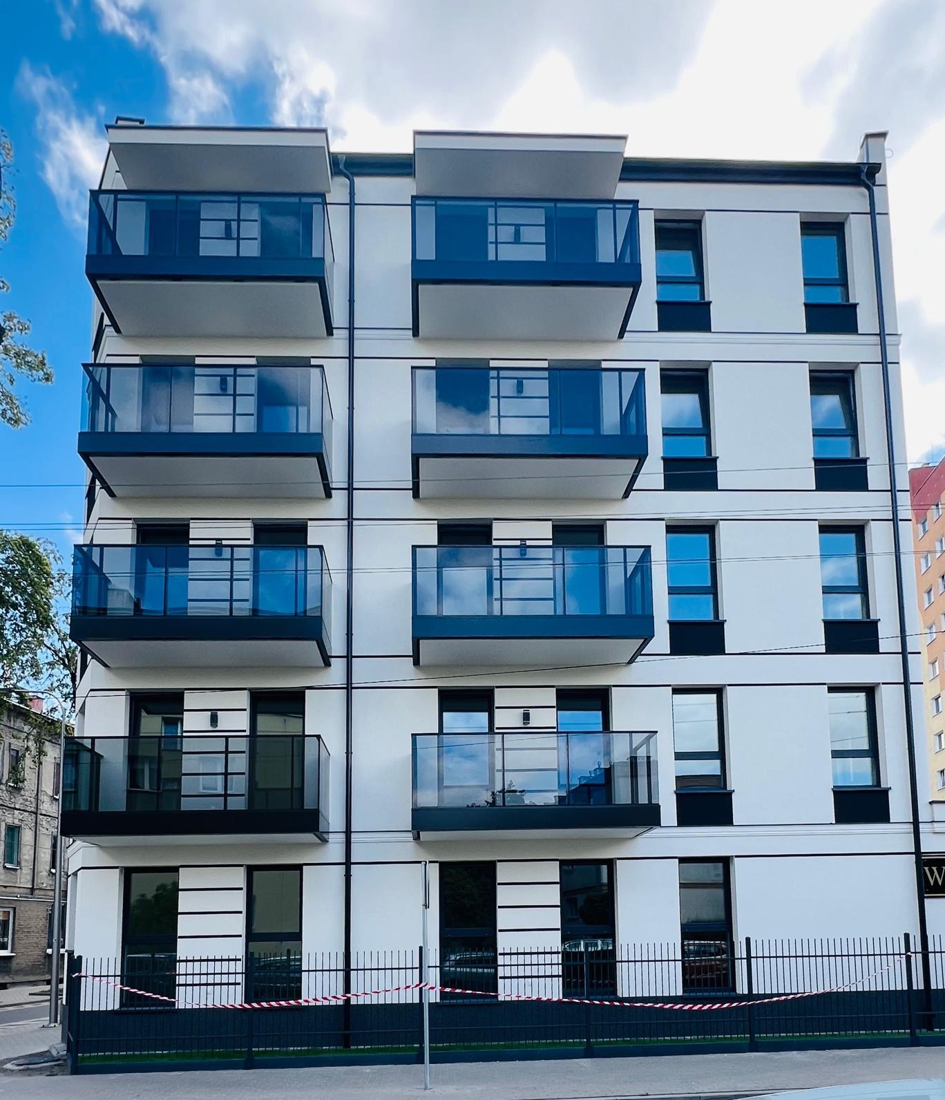 Nowoczesny budynek mieszkalny z balkonami z balustradami szklanymi, widok z dołu, zabezpieczony taśmą ostrzegawczą.