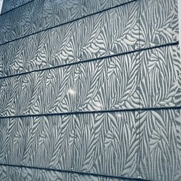 Royal Firany - Szara roleta rzymska z wzorem liści, widoczne sznurki do podnoszenia, zamontowana w oknie.