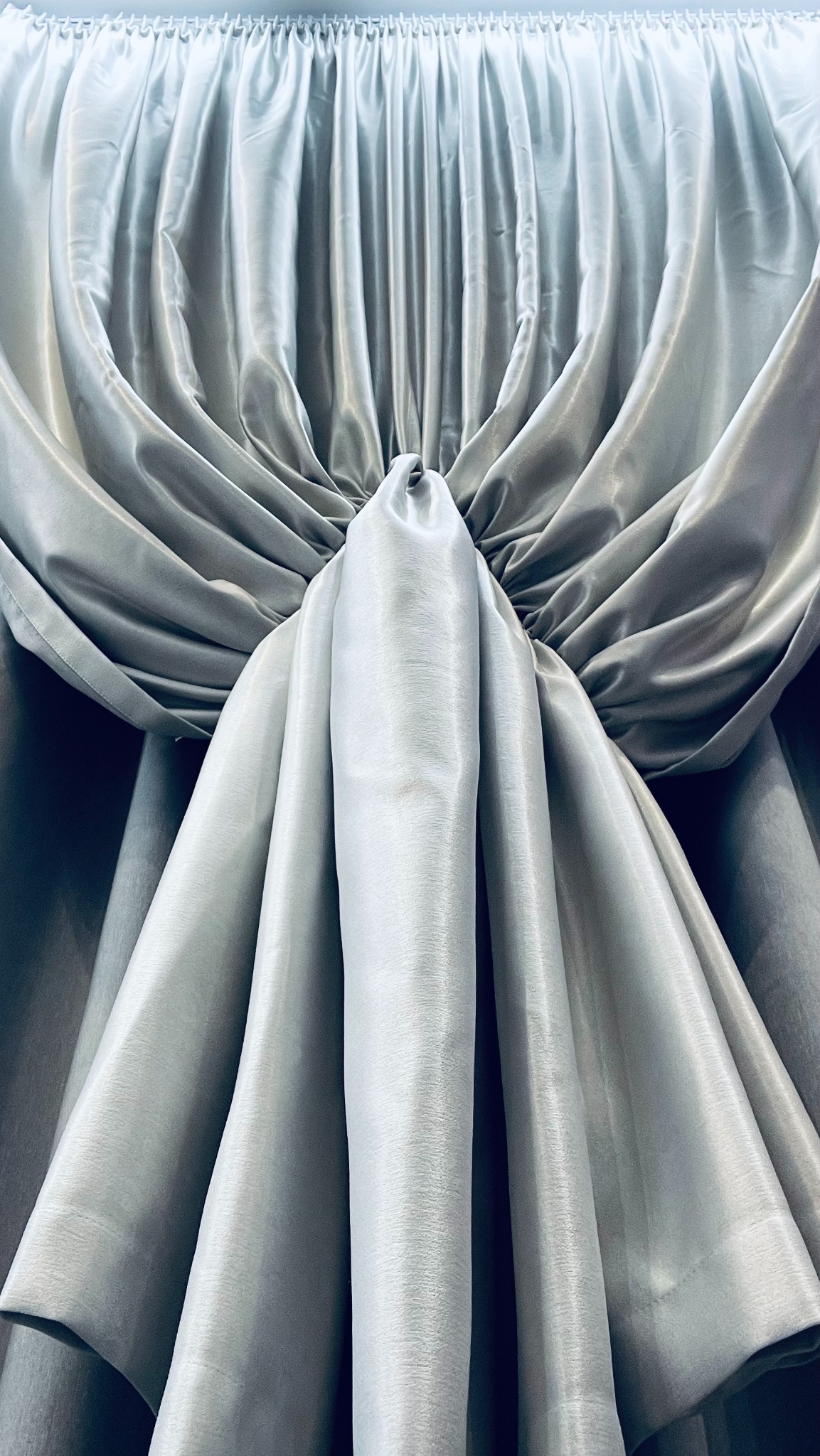 Elegancka, srebrzysta zasłona z marszczeniem u góry, upięta w dekoracyjny węzeł, tworząca miękkie fałdy i subtelne cienie.