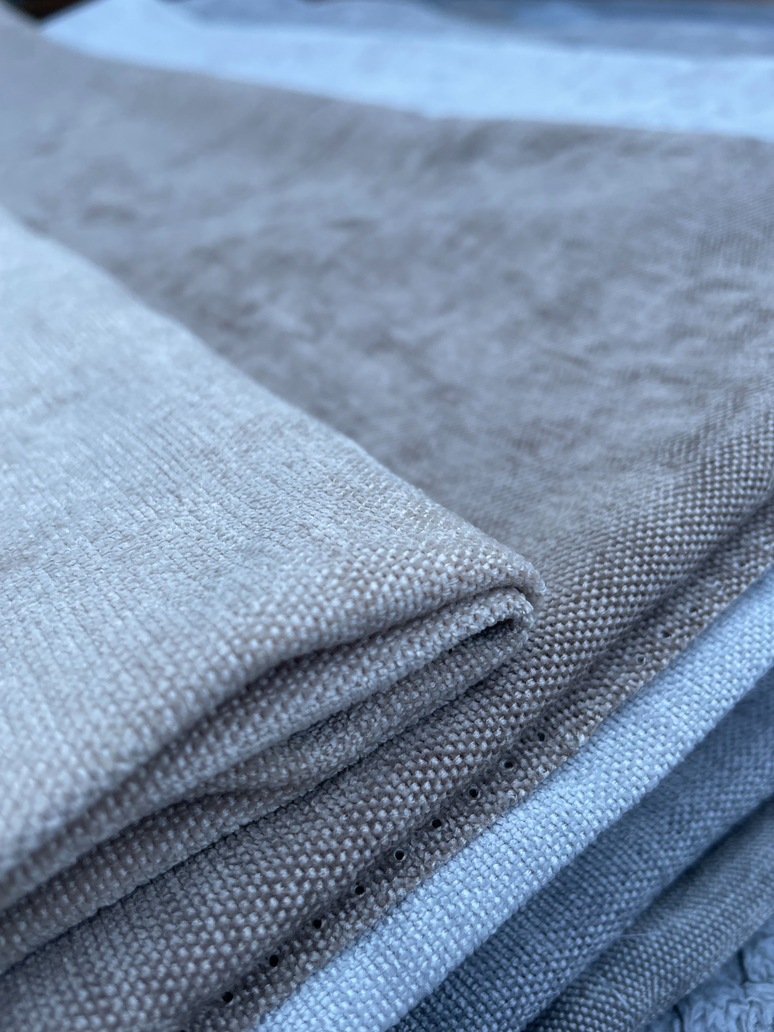 Stos beżowych i szarych tkanin o wyraźnej fakturze, ułożonych warstwami, z widocznym splotem włókien.