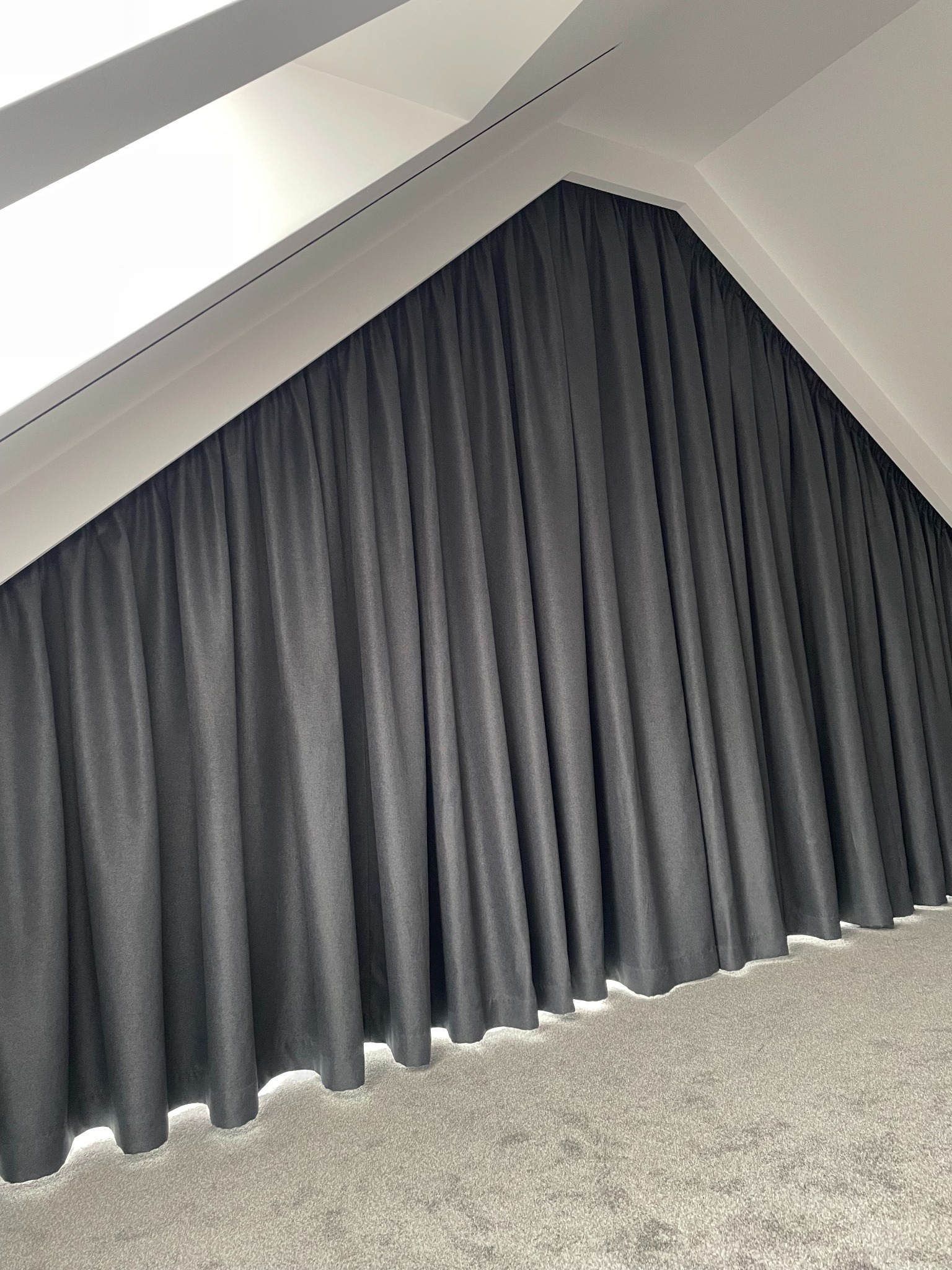 Ciemne zasłony wkomponowane w skos dachu, tworzące przytulną atmosferę w pomieszczeniu. Minimalistyczny design i stonowana kolorystyka.