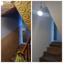 Klatka schodowa przed i po malowaniu: po lewej stara, beżowa ściana z drewnianą boazerią sufitową w ozdobne heksagony, po prawej świeżo pomalowana na szaro ściana i schody zabezpieczone folią...