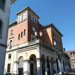 Foto Pablo Paweł Osiński - Elewacja budynku poczty z cegły i piaskowca, z arkadami wejściowymi, zegarem na wieżyczce i ozdobnymi latarniami.